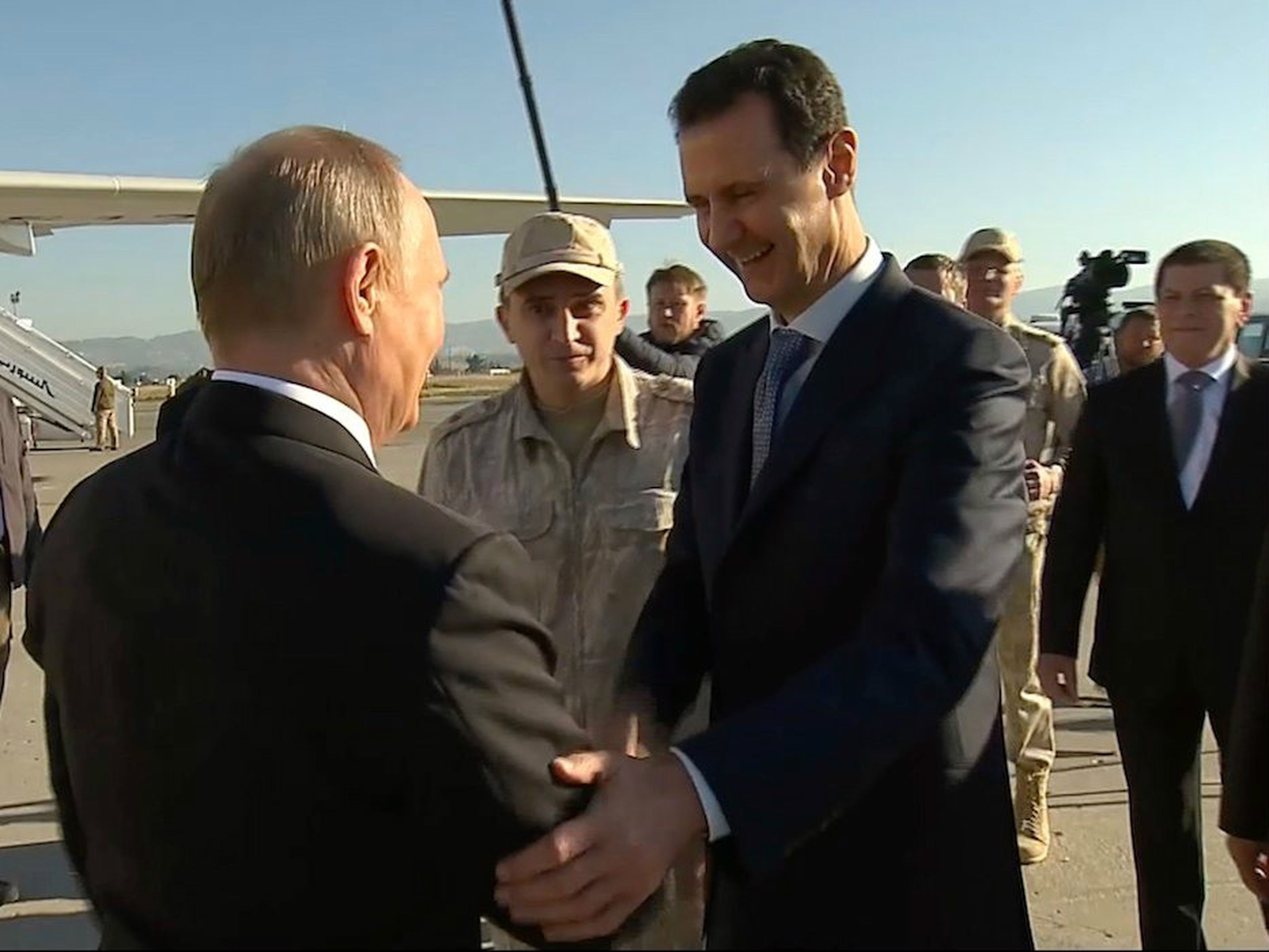 Captura de un reportaje de televisión en el que se ve (de der. a izqd.) al presidente de Siria, Bashar al-Ásad, saludando al presidente de Rusia, Vladimir Putin, en la base áerea siria de Hemeimeem el 11 de diciembre de 2017.