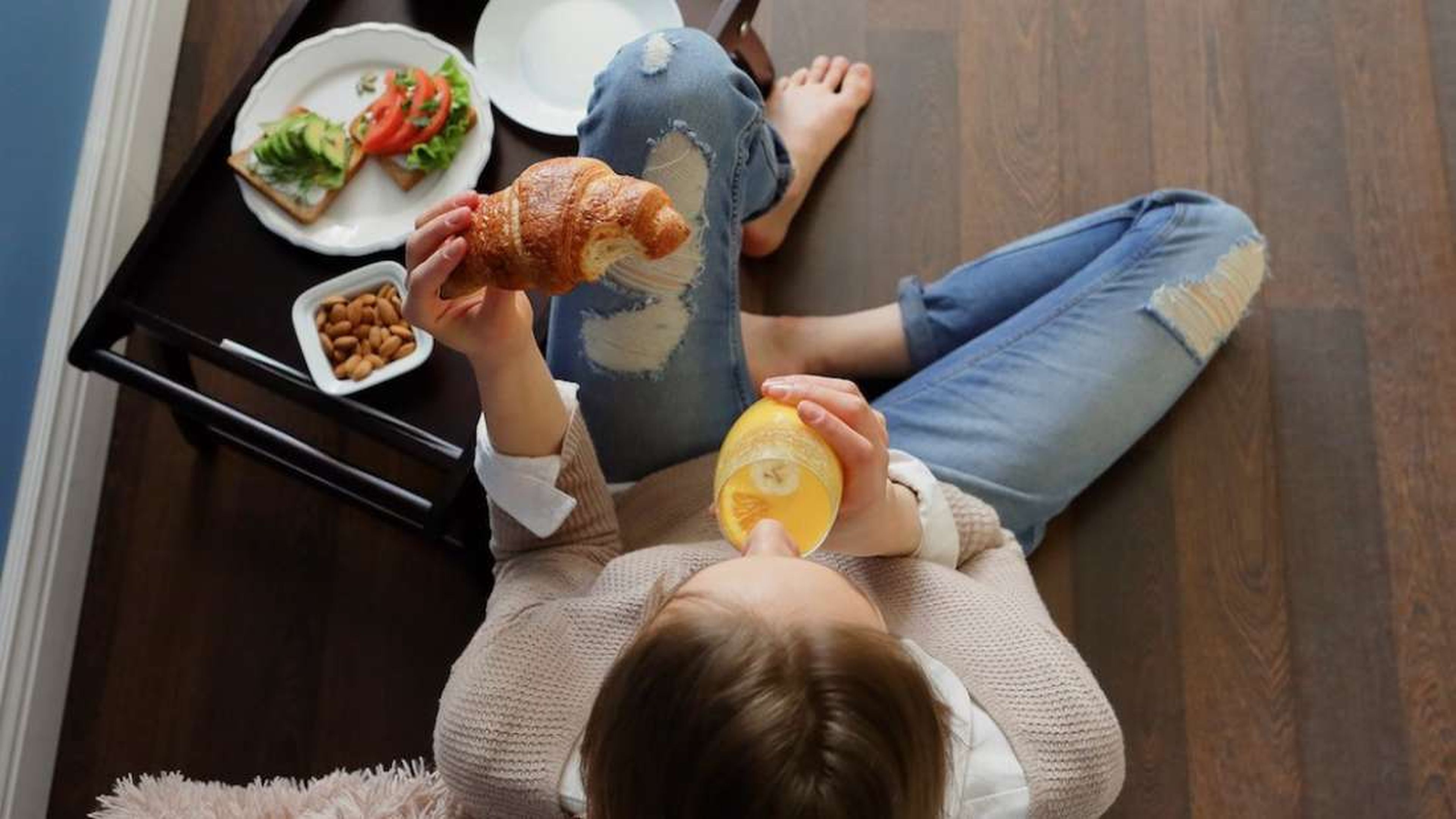 Una mujer desayunando croissant y zumo de naranja