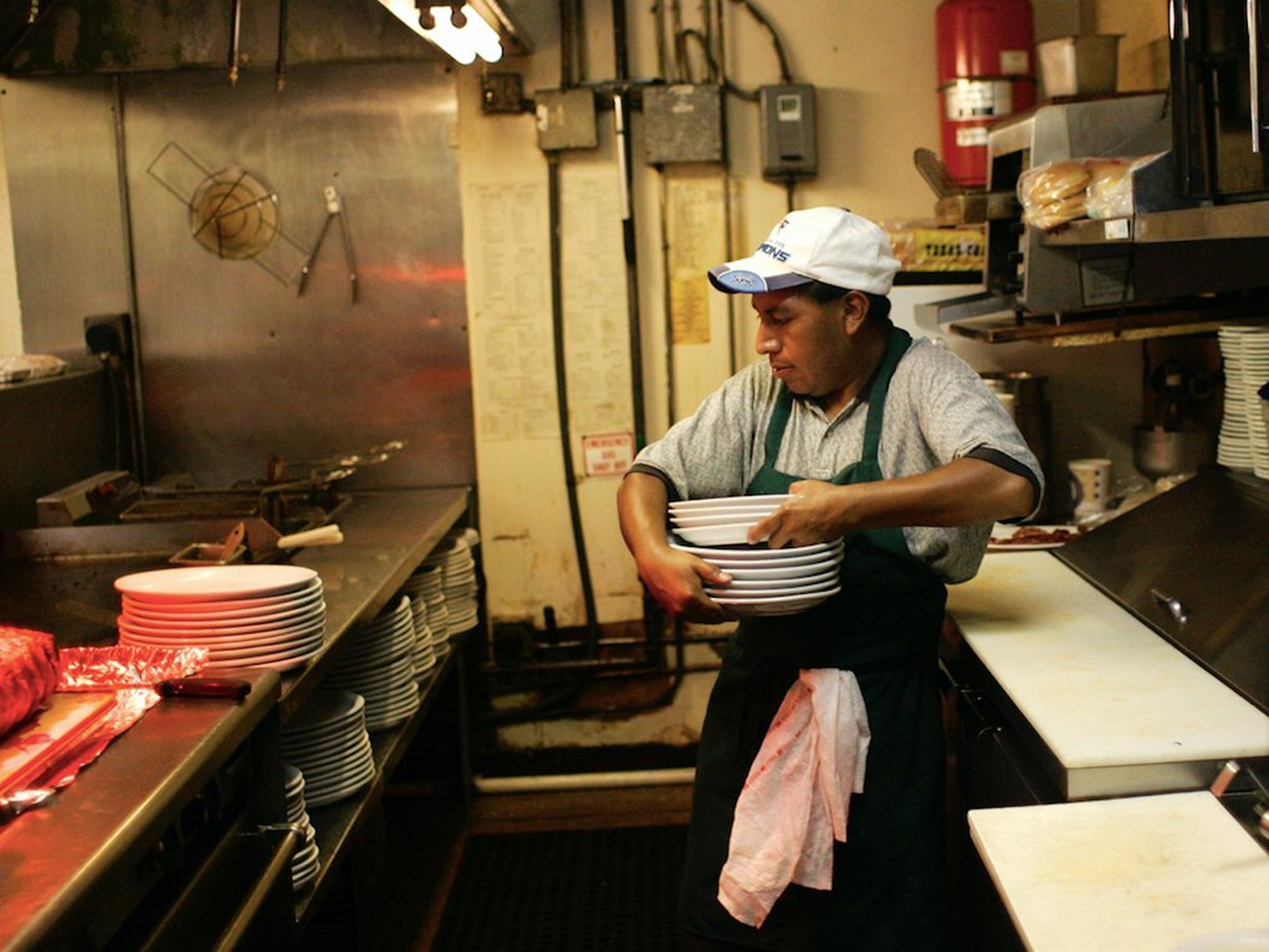 Persona de origen latino lava platatos en la cocina de un restaurante