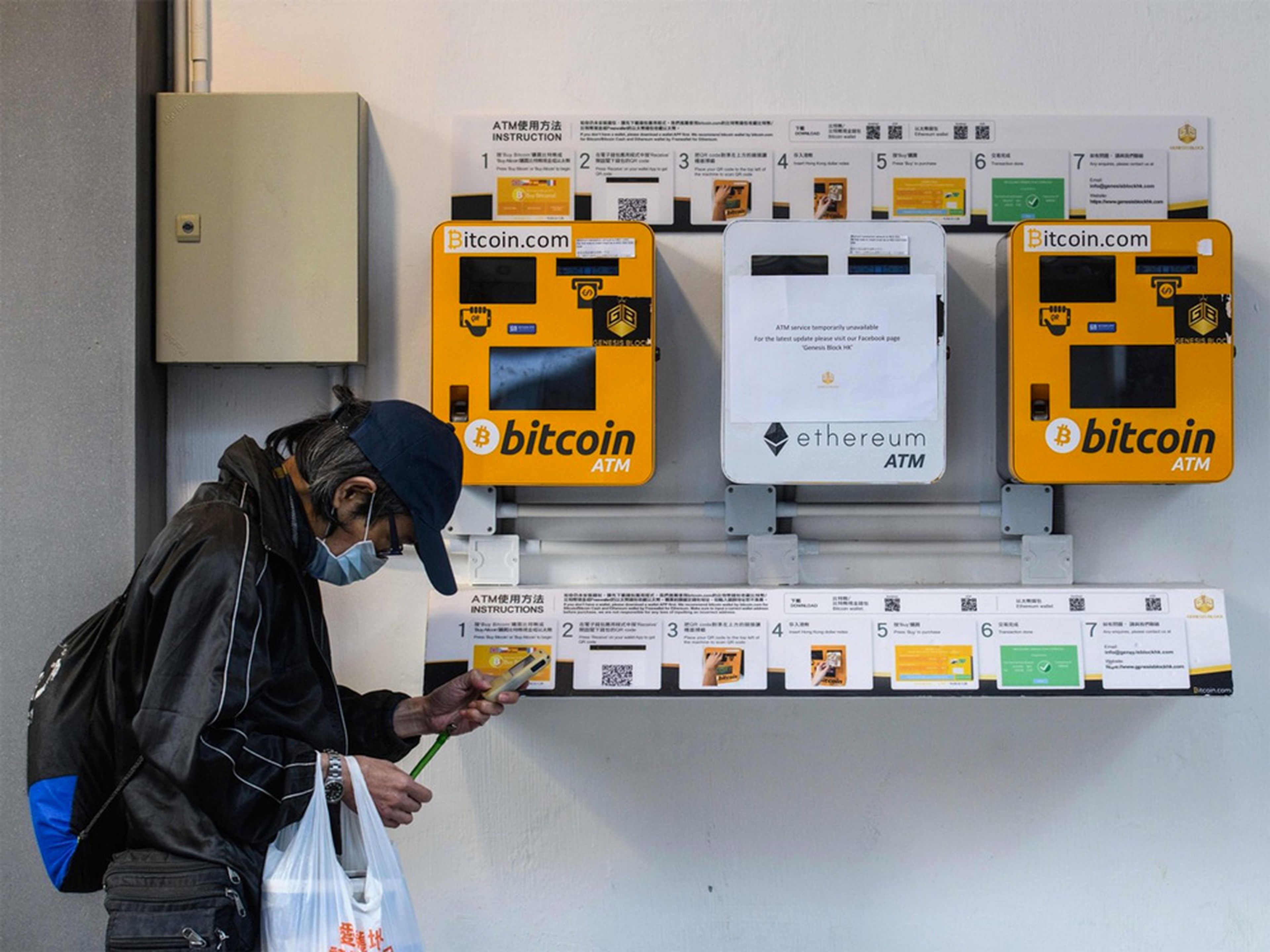 Un hombre utiliza su teléfono mientras pasa junto a un cajero de criptomonedas de Bitcoin y Ethereum en Hong Kong.