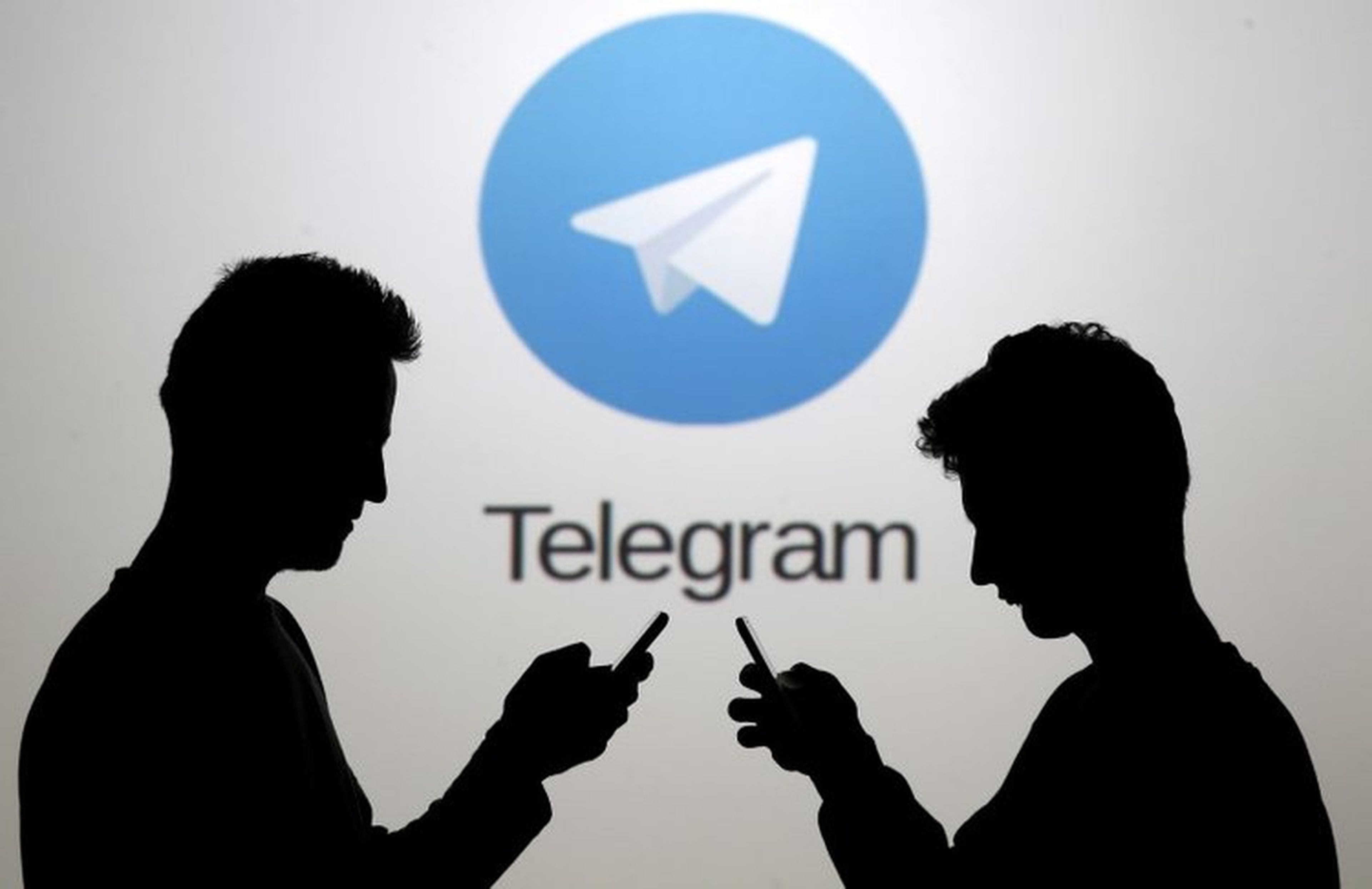 Dos hombres posan junto a sus 'smartphone' frente a una pantalla que muestra el logotipo de Telegram.