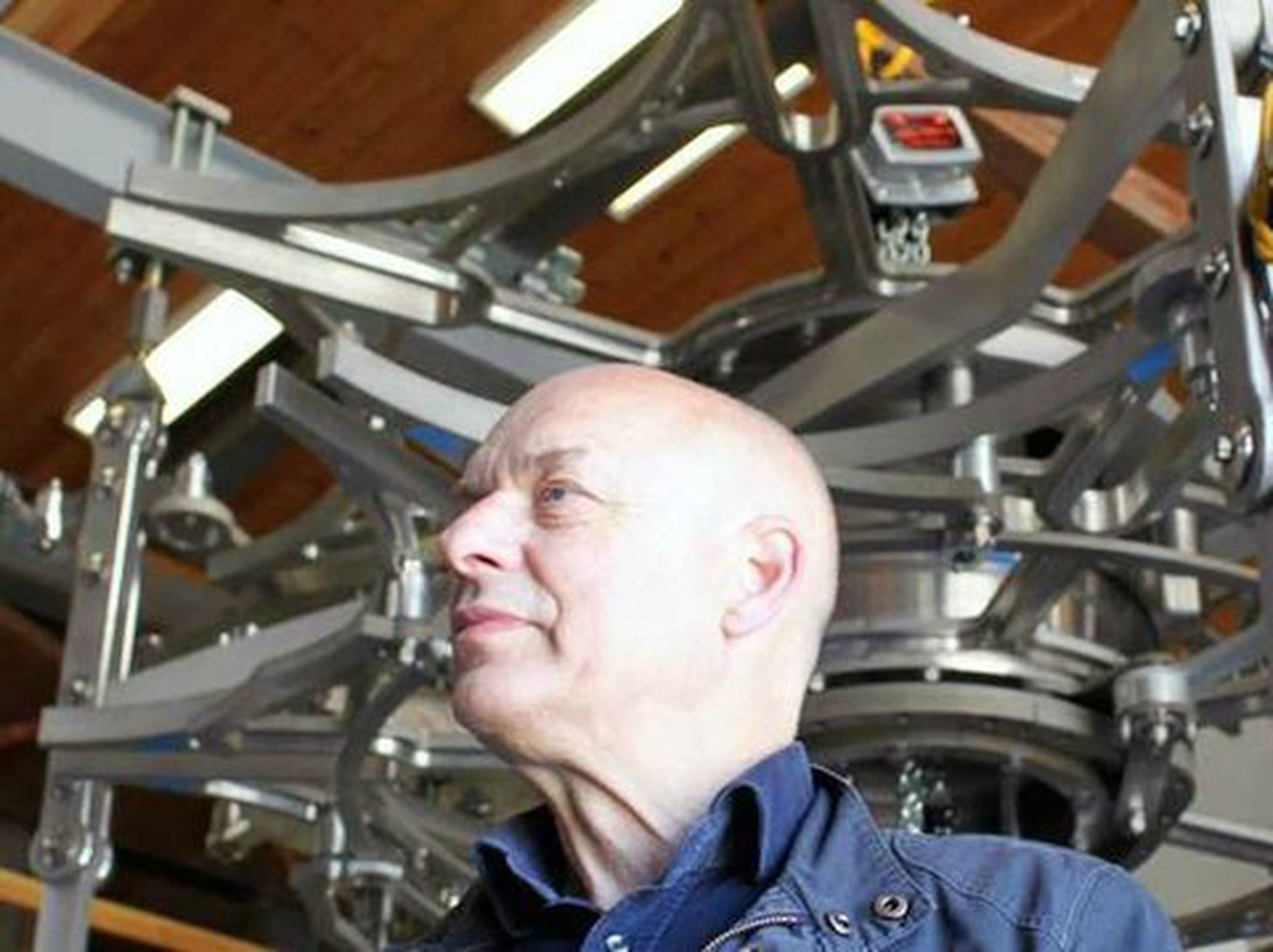 Brian Eno supervisa los mecanismos del reloj gigante apoyado por Jeff Bezos dentro de una montaña.