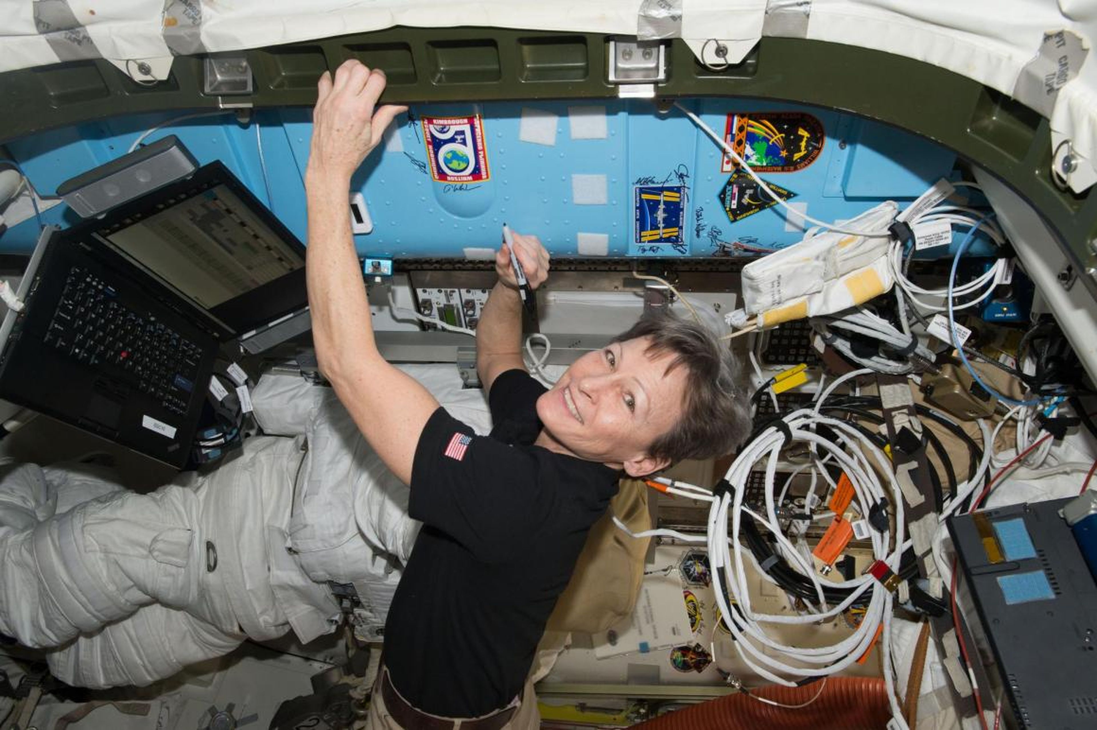 NASA astronaut Peggy Whitson signs a bulkhead on the International Space Station next to the Expedition 50 crew patch in 2017.