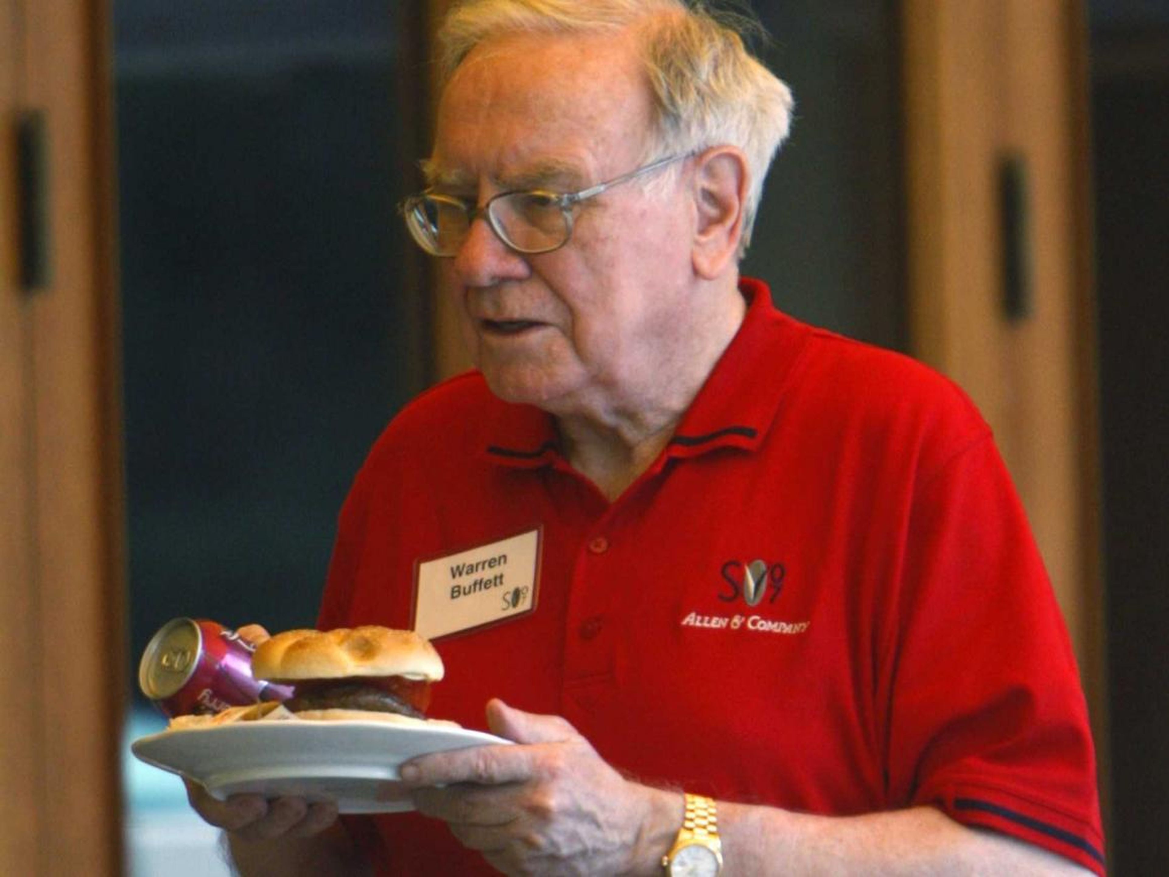 El multimillonario Warren Buffett con una hamburguesa y una bebida en la mano.