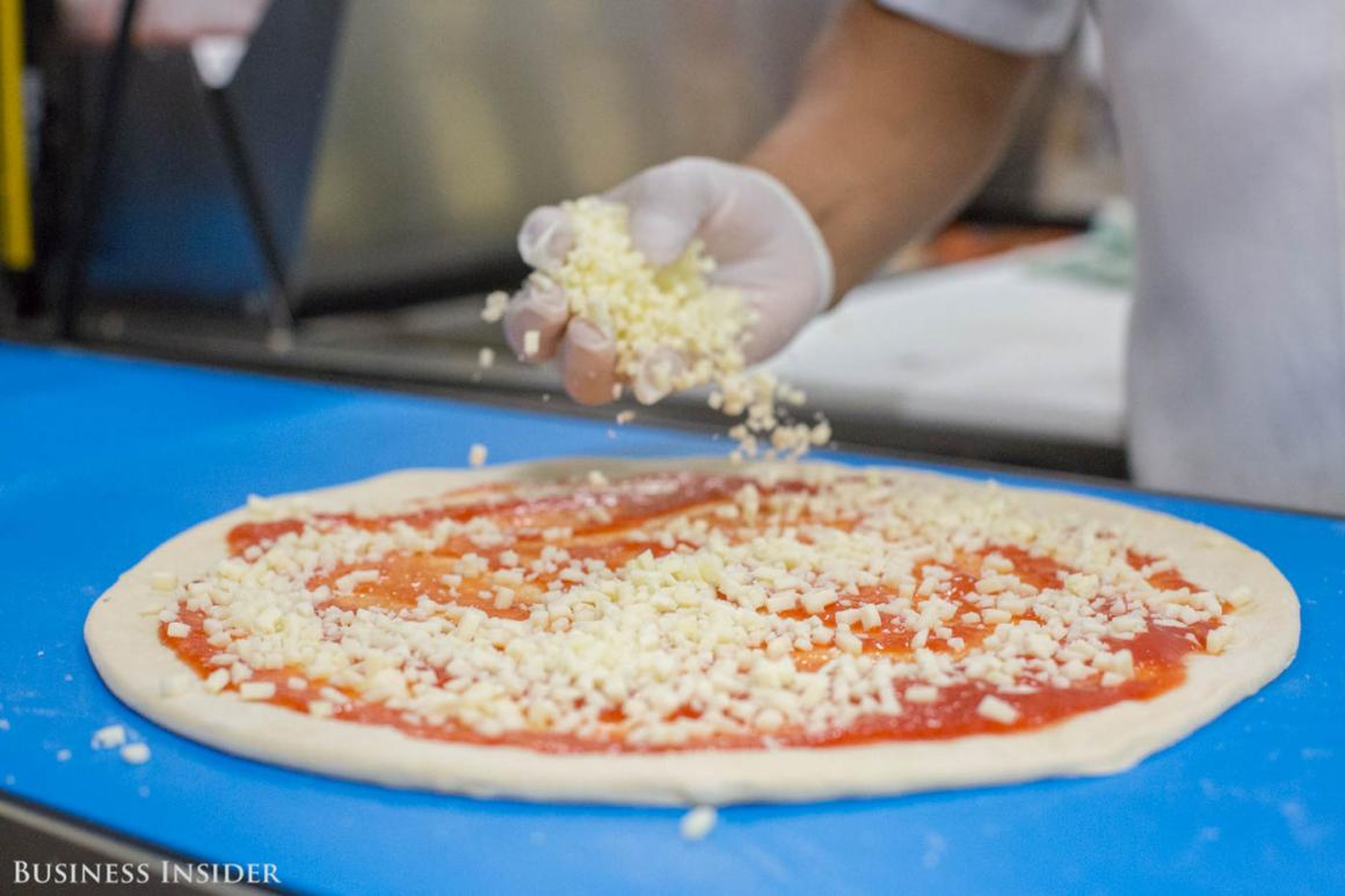 A human dresses the pie with cheeses and toppings. It's a difficult part of the process to automate because toppings come in different weights, sizes, and textures.