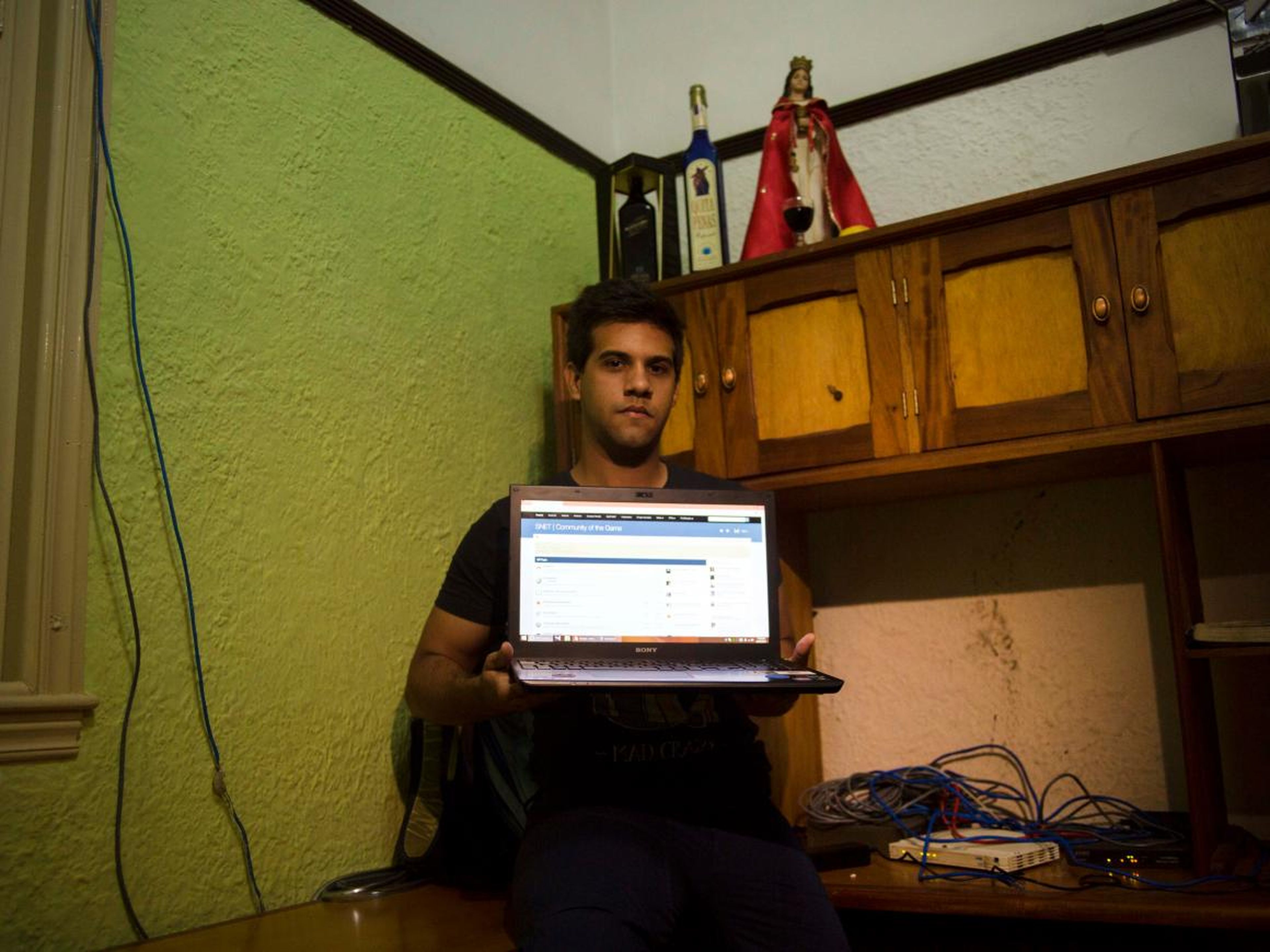 Rafael Antonio Broche Moreno posa con su ordenador, módem y su red por cable en su casa de La Habana.