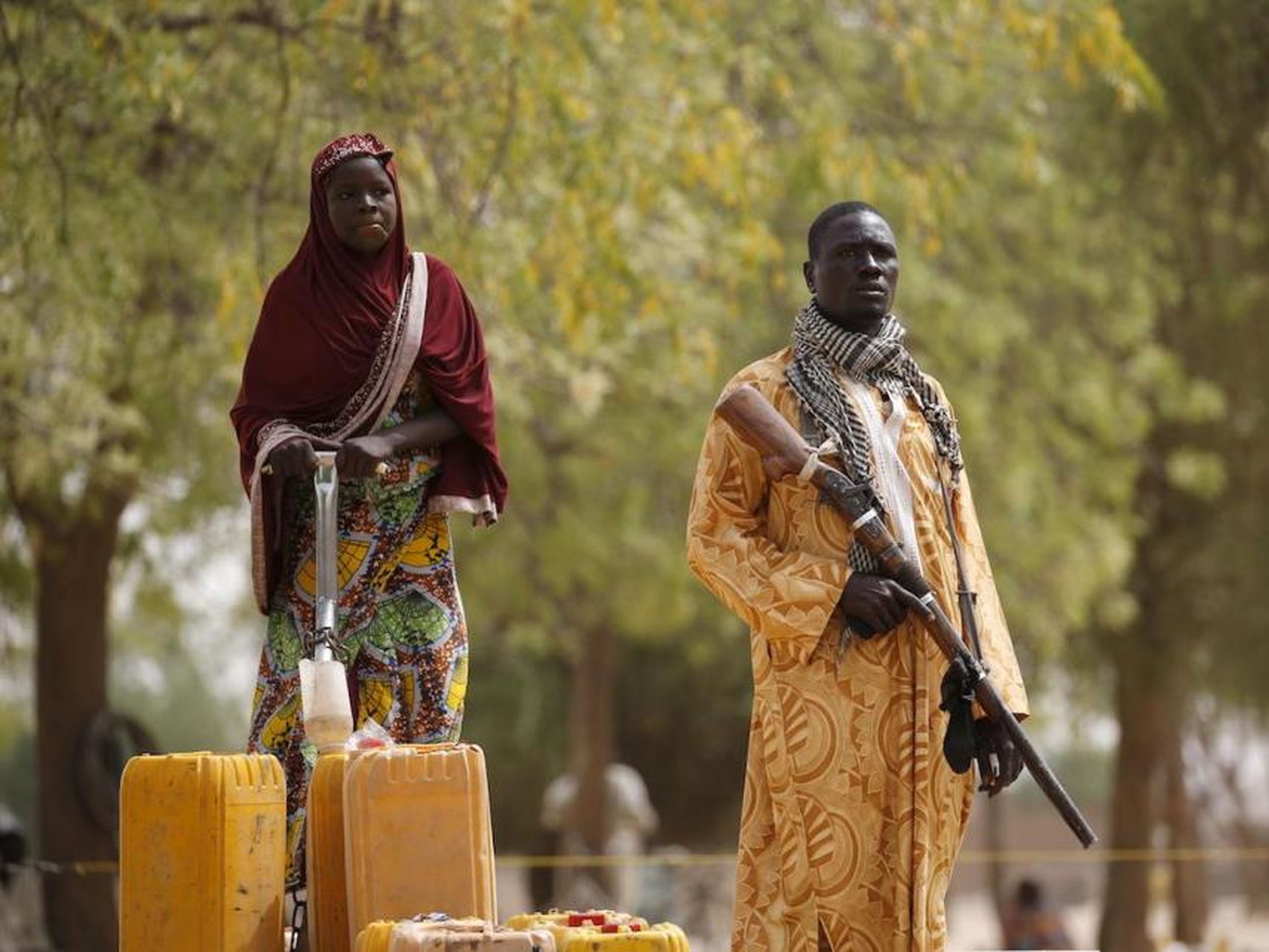 Un miembro de un grupo de vigilantes civiles sostiene un rifle de caza mientras una mujer bombea agua en bidones en Kerawa, Camerún, 16 de marzo de 2016.