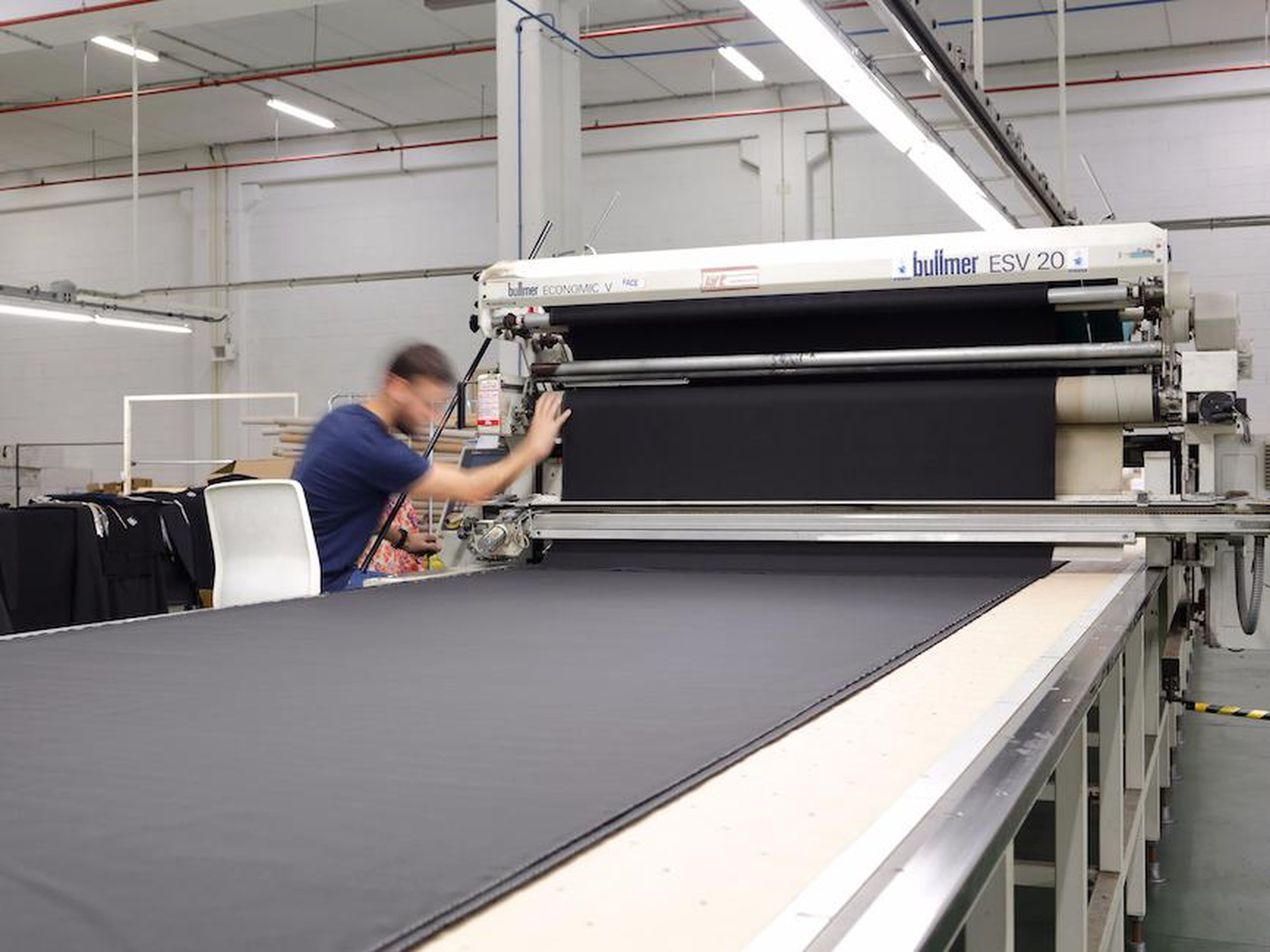 The fabric is laid out under large cutting machines, and the paper is placed on top.