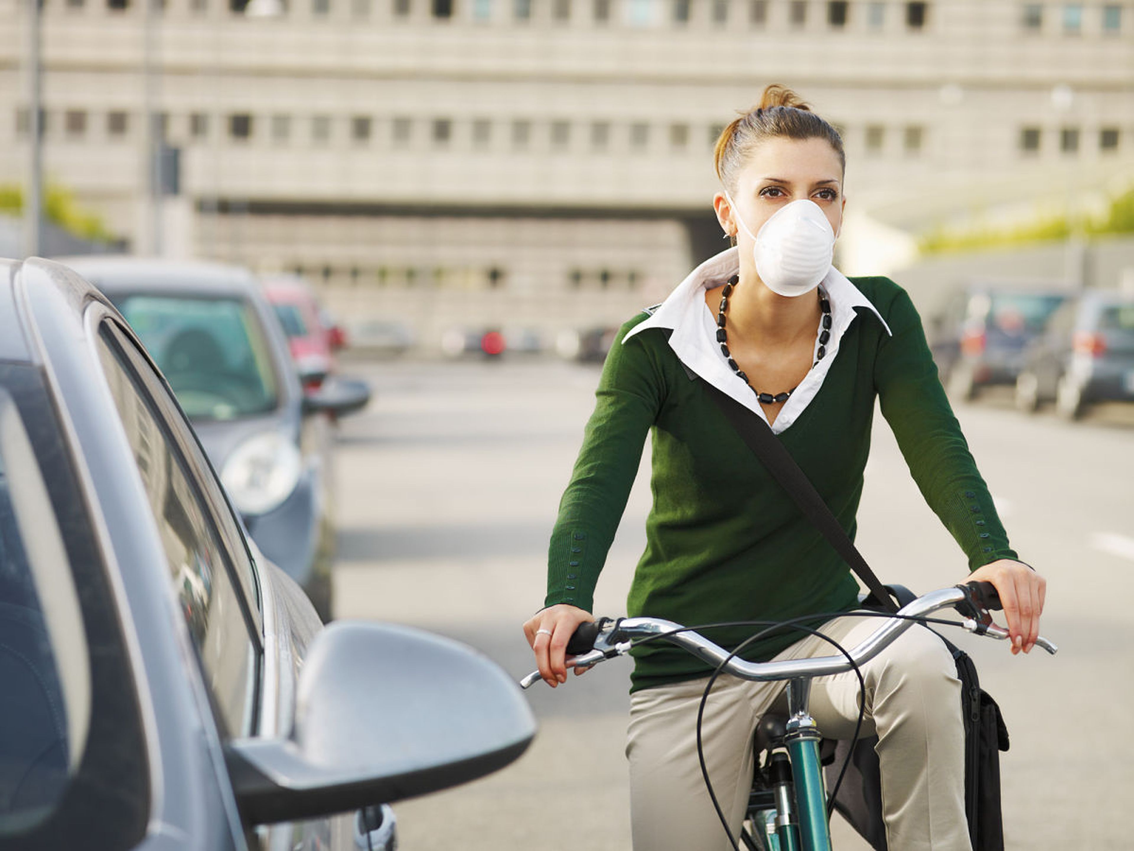 Una mujer utiliza una máscara respiratoria mientras transita en bicicleta.