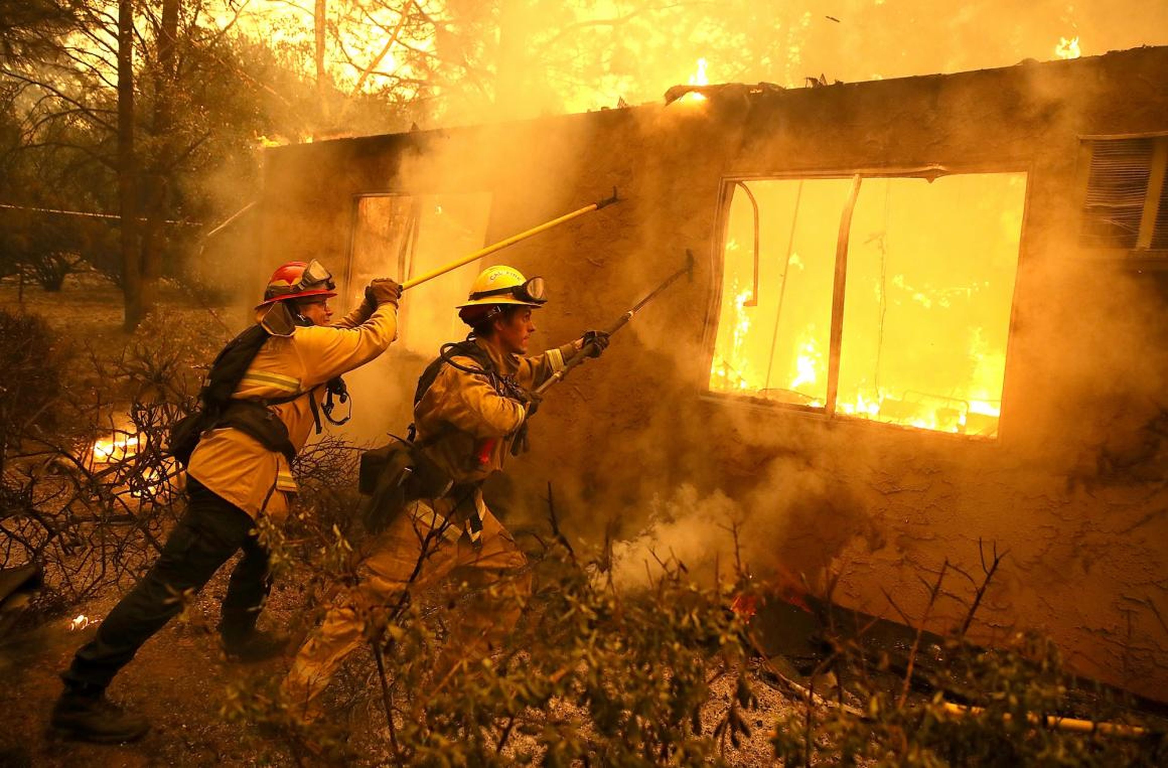 Firefighters try to keep flames from a burning home from spreading to a neighboring apartment complex as they battle the Camp Fire on November 9, 2018 in Paradise, California.