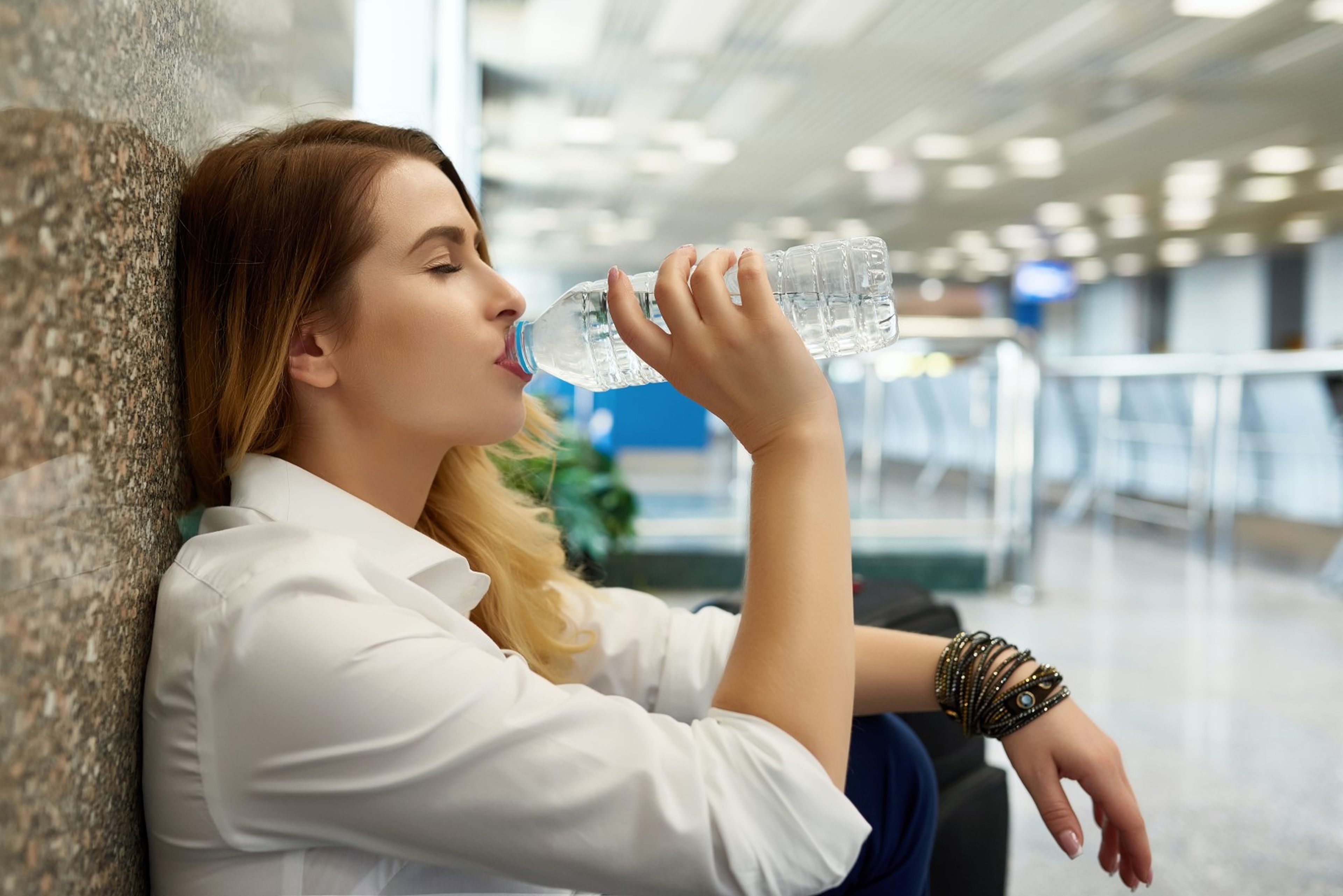 Una chica bebe agua de una botella de plástico en un aeropuerto