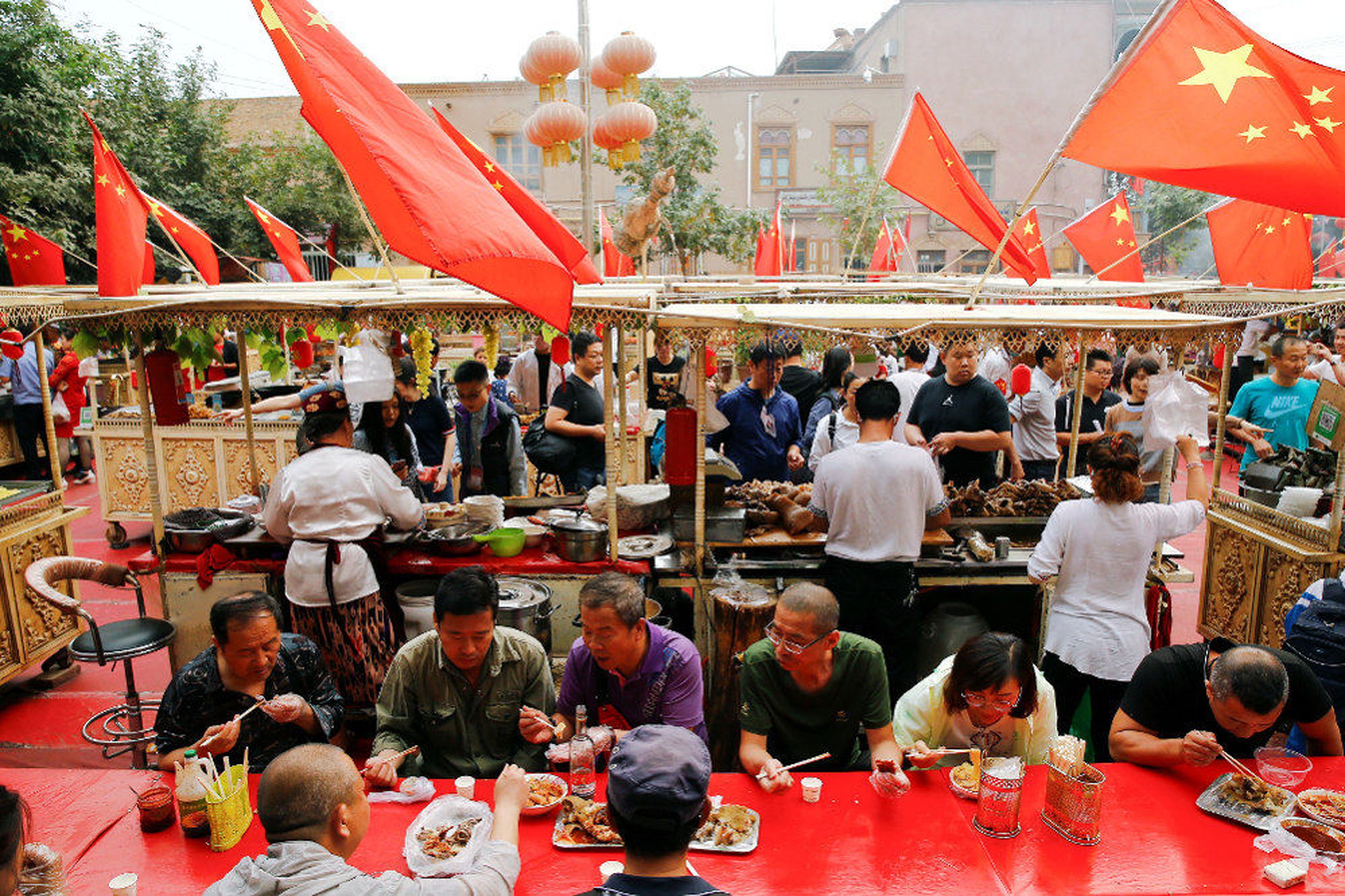 La gente come bajo las banderas nacionales chinas en la Ciudad Vieja en Kashgar
