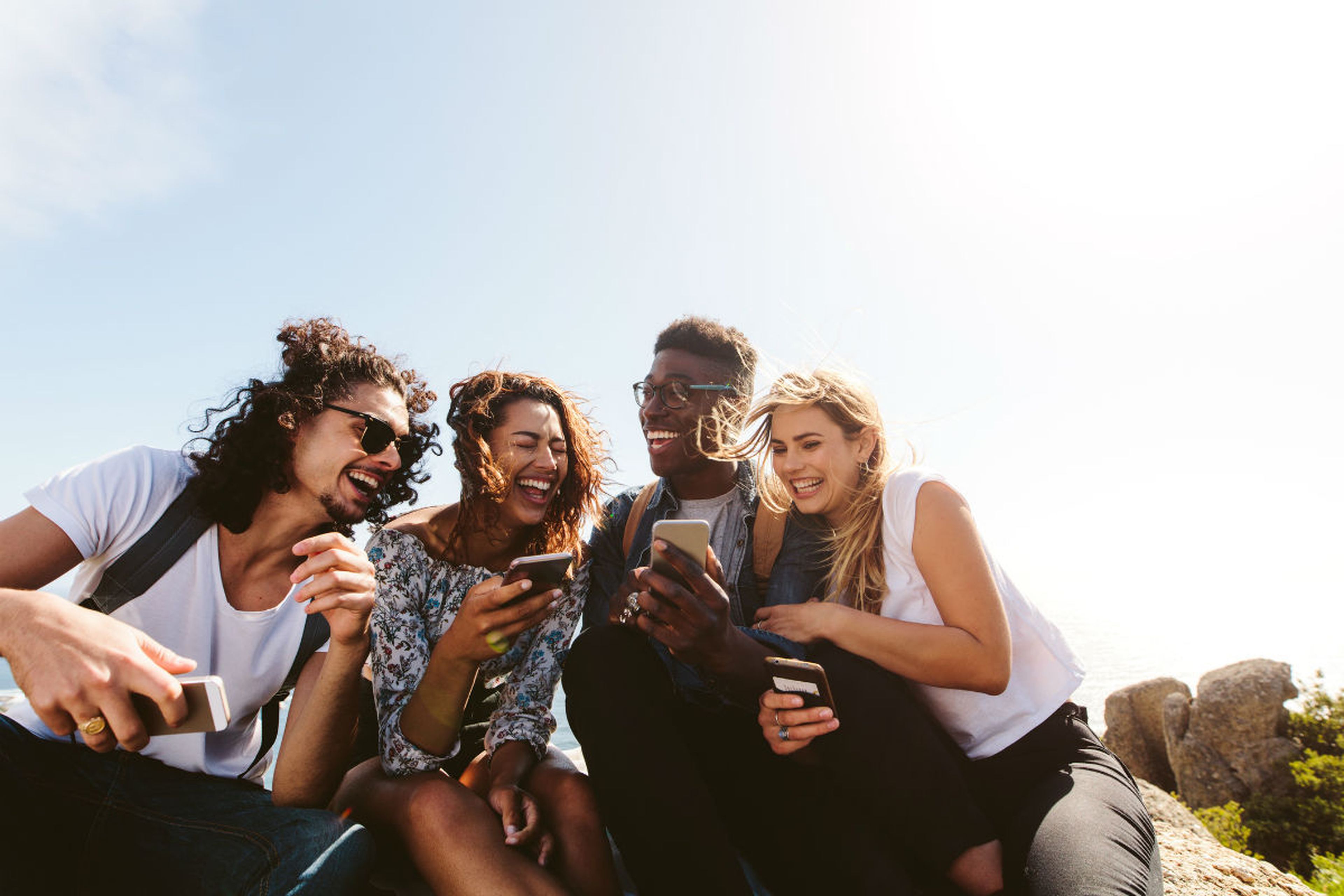 Cuatro millennials se ríen mientras se relacionan con sus smartphones.