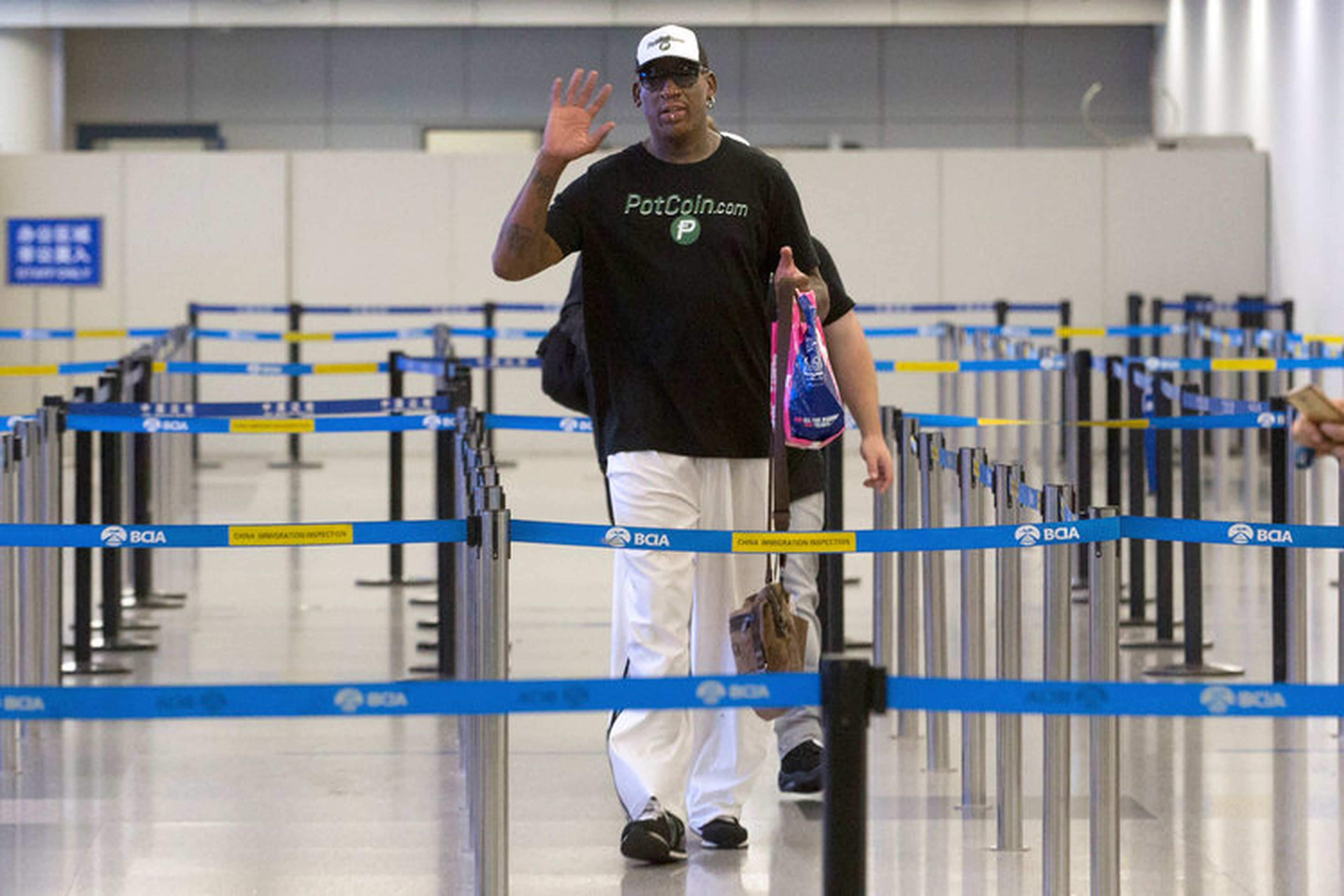 Rodman saluda a los fotógrafos mientras se prepara para pasar el control de inmigración en el Aeropuerto Internacional de Pekín, martes, 13 de junio de 2017.
