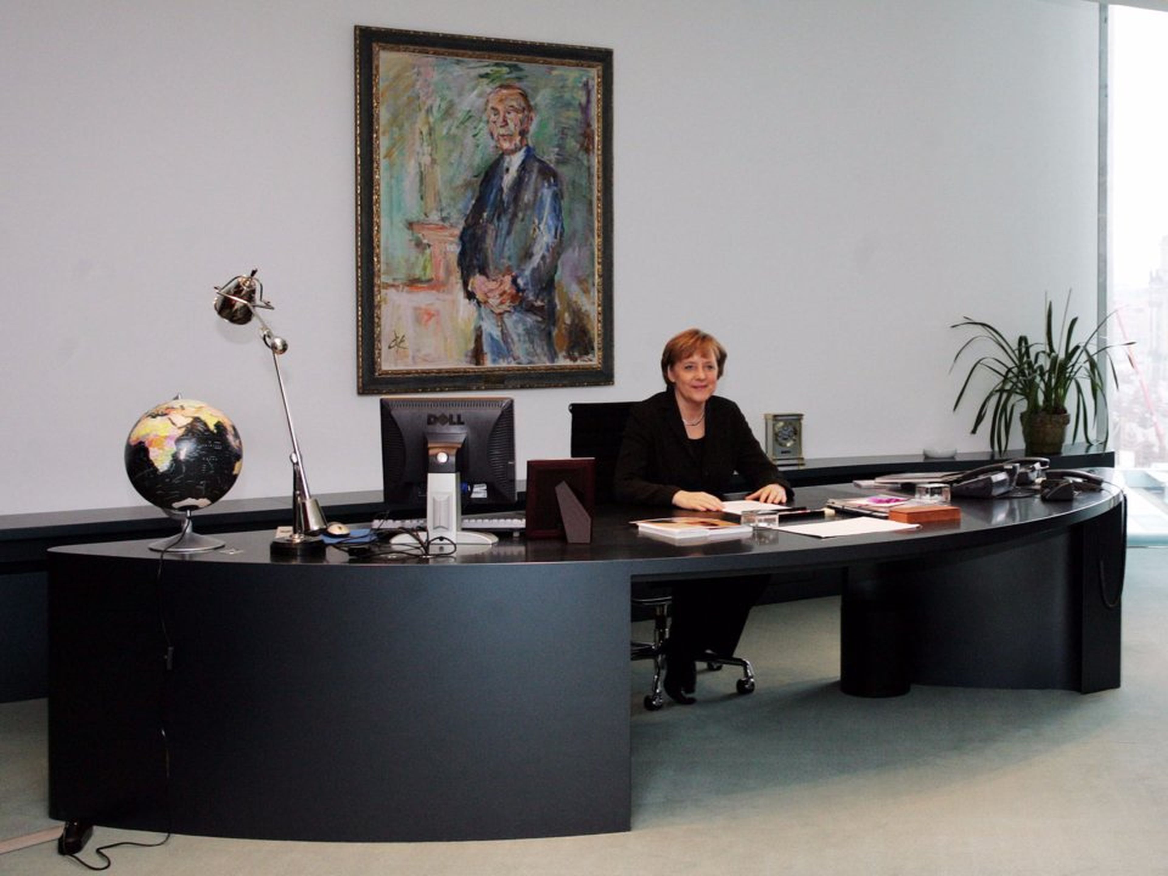 La canciller alemana, Angela Merkel, se sienta en su escritorio en su despacho de la cancillería de Berlín en 2006, frente a una pintura del primer canciller alemán, Konrad Adenauer.
