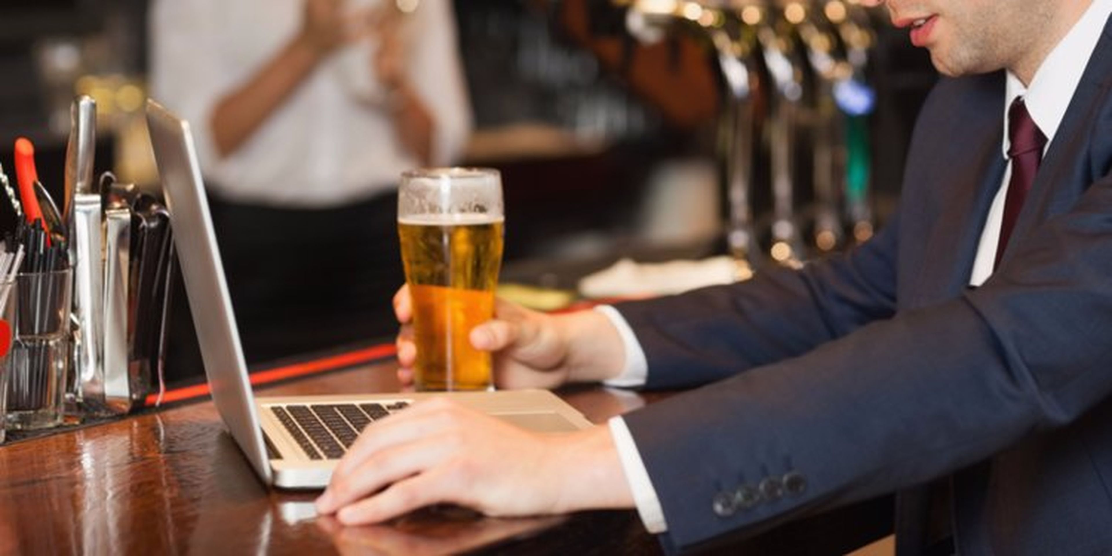 hombre bebiendo una cerveza y trabajando con su portátil en la barra de un bar