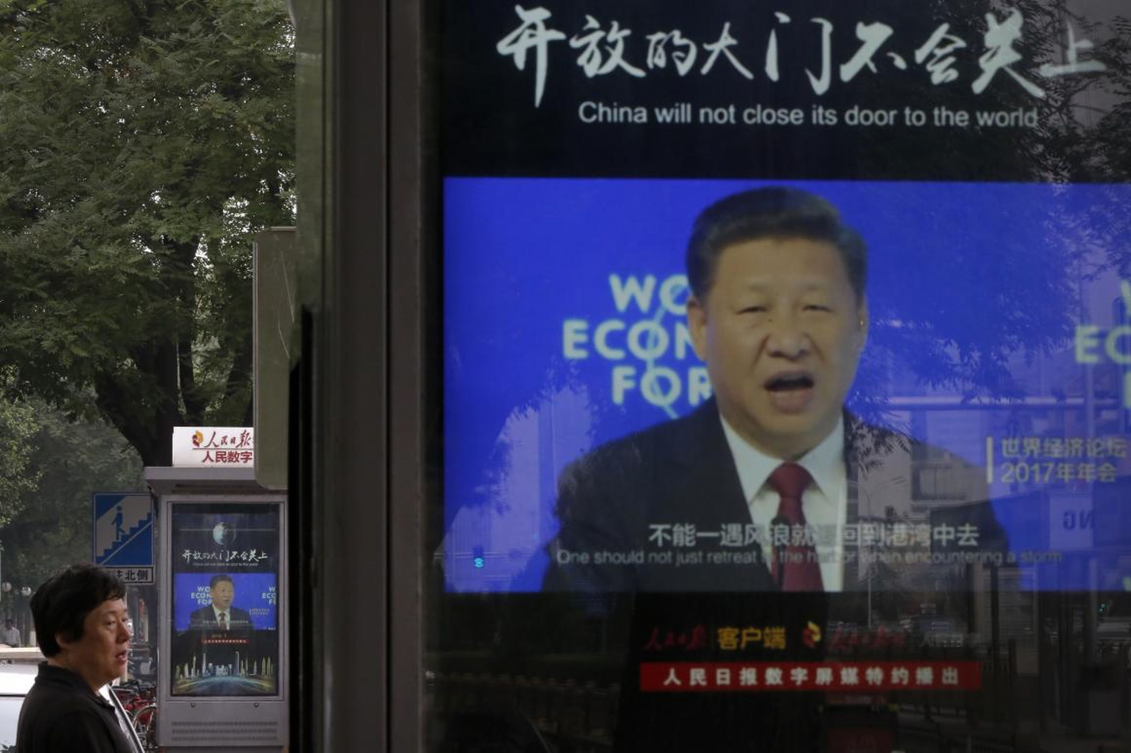 A man walks by electronic display panels advertising a video footage of Chinese President Xi Jinping speaking at the World Economy Forum on a street in Beijing, Monday, June 25, 2018.