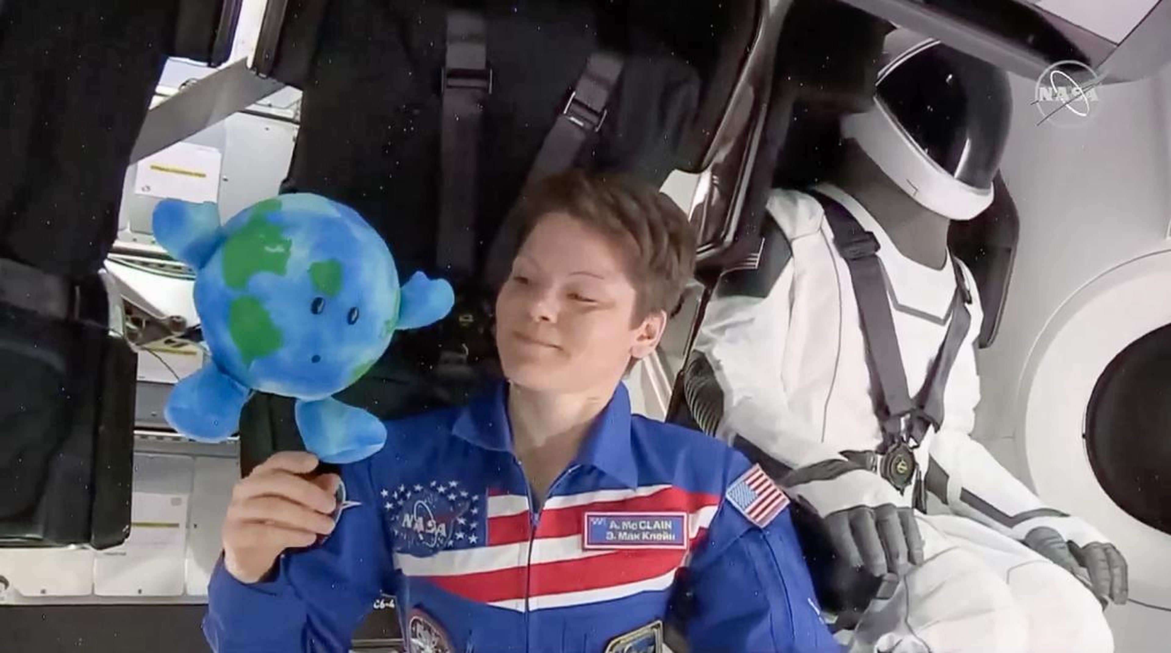 Astronaut Anne McClain plays with a plush Earth toy inside SpaceX's Crew Dragon capsule.