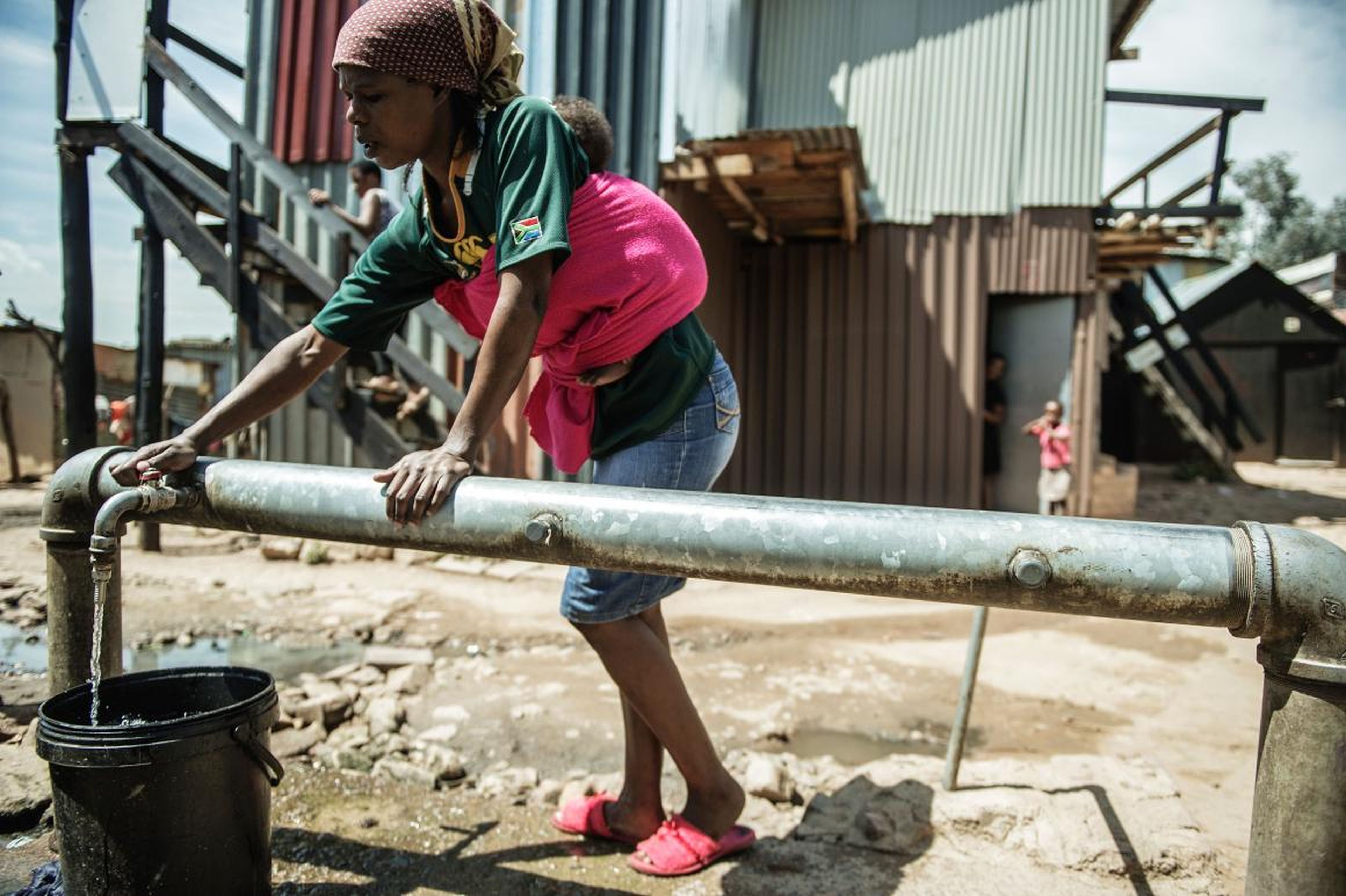 Una mujer recolecta agua de uno de los pocos grifos de agua comunales disponibles para las miles de personas que viven en el asentamiento informal Zandspruit en Johannesburgo, Sudáfrica.