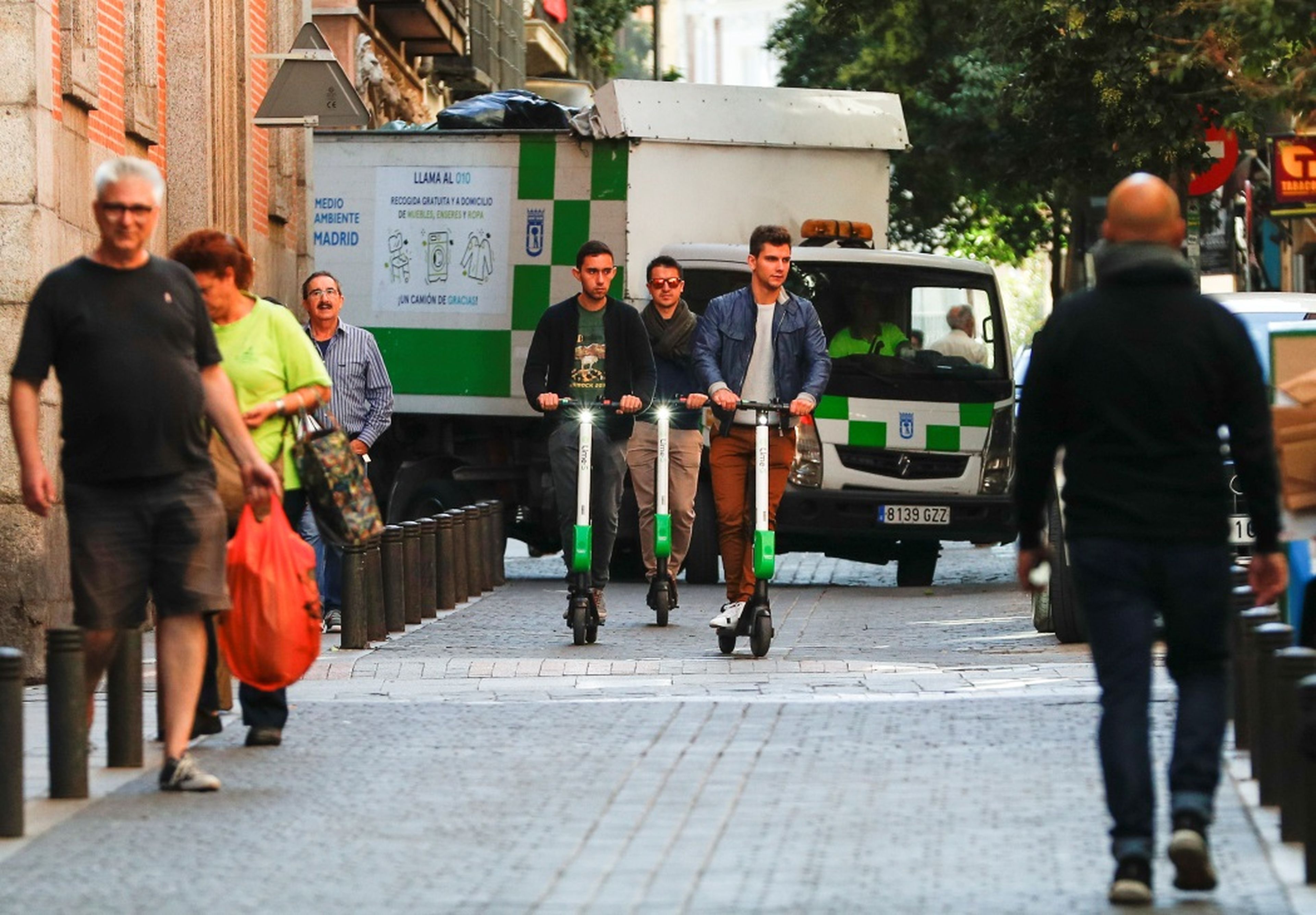 Tres jóvenes usan patinetes eléctricos compartidos de Lime en Madrid.