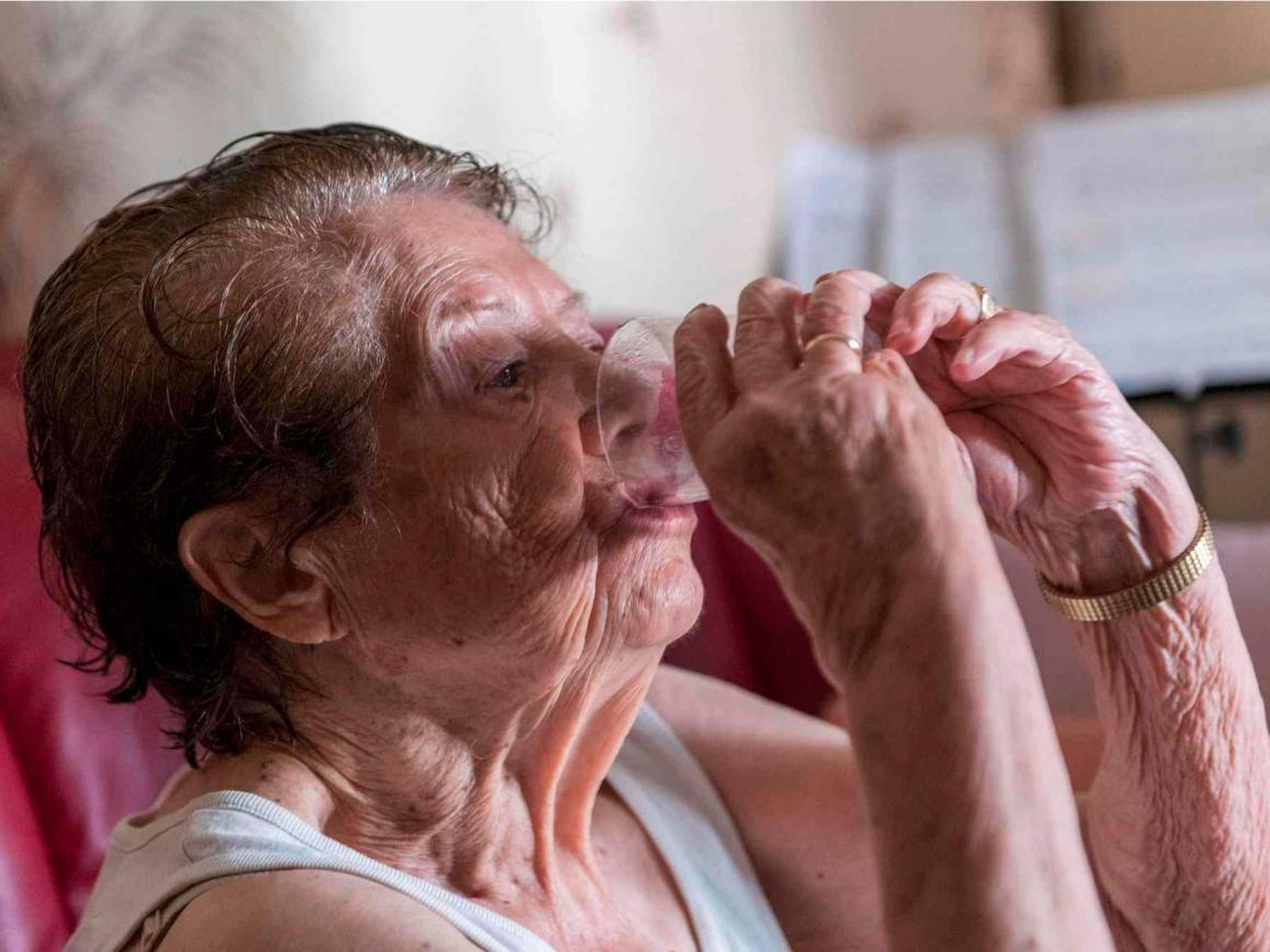 An elderly person drinks a glass of water.