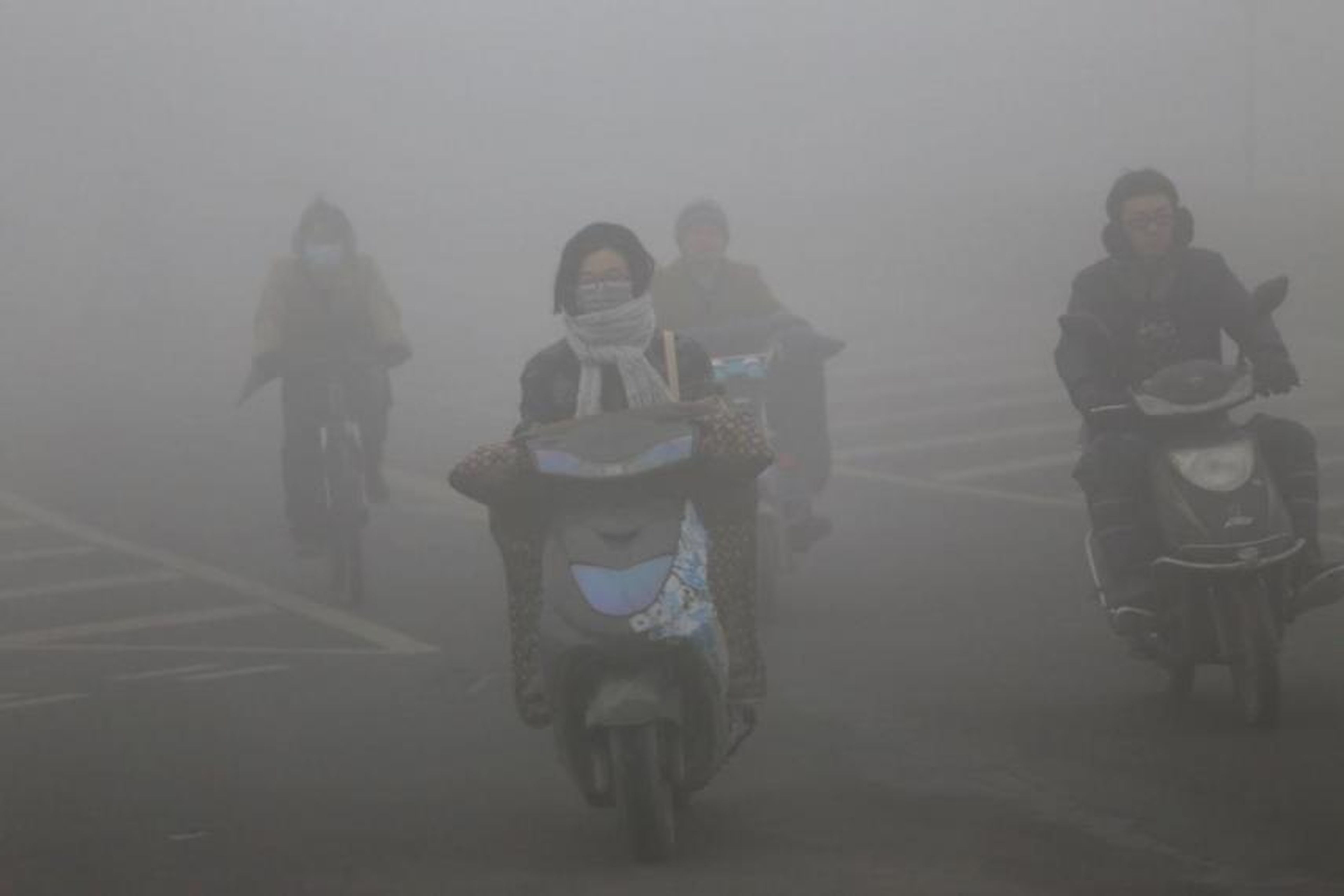 Ciclistas con máscaras viajan por una carretera con mucha niebla tóxica el 23 de diciembre de 2015 en Zhengzhou, China.