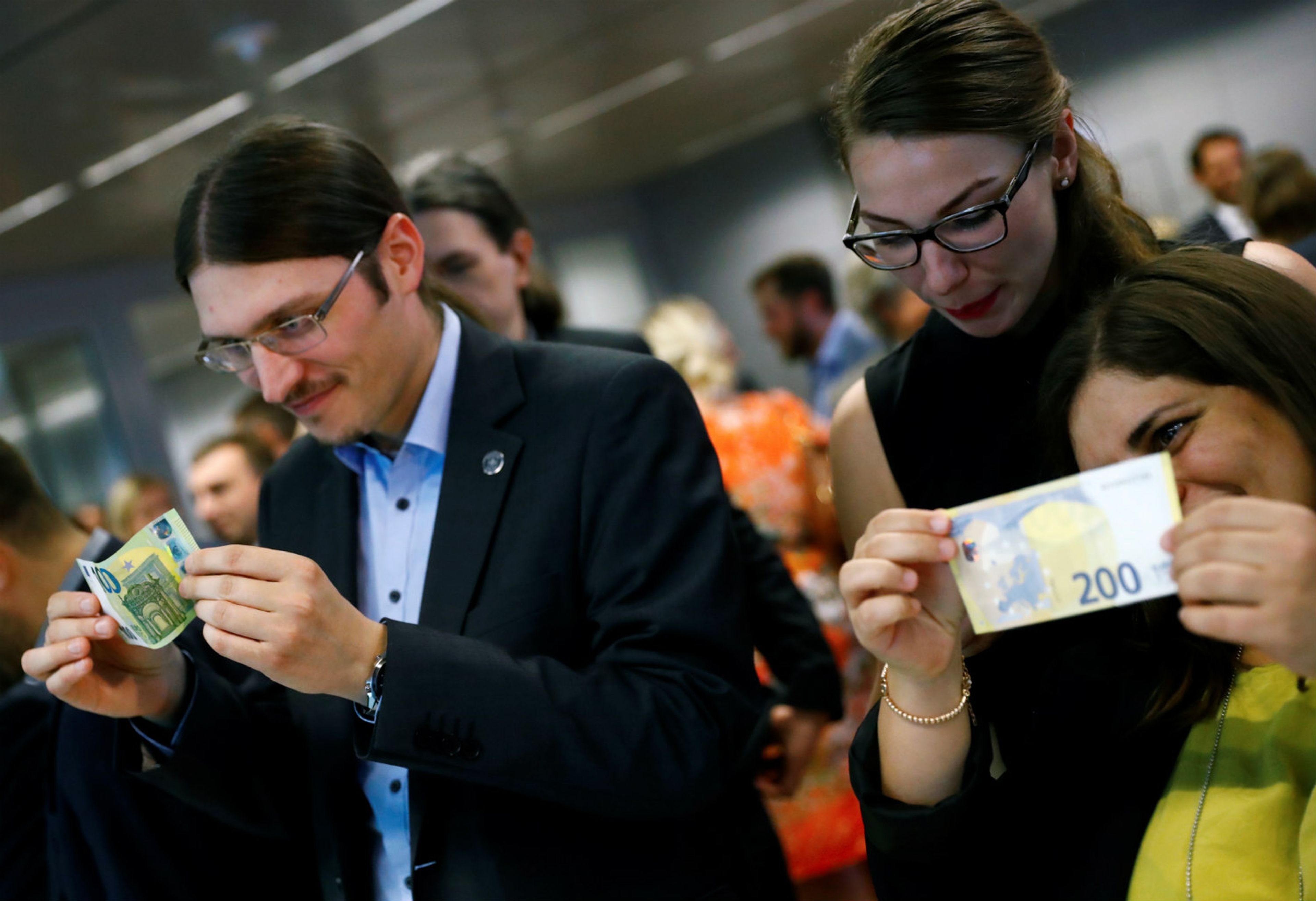 Gente tocando los nuevos billetes de 100 y 200 euros.