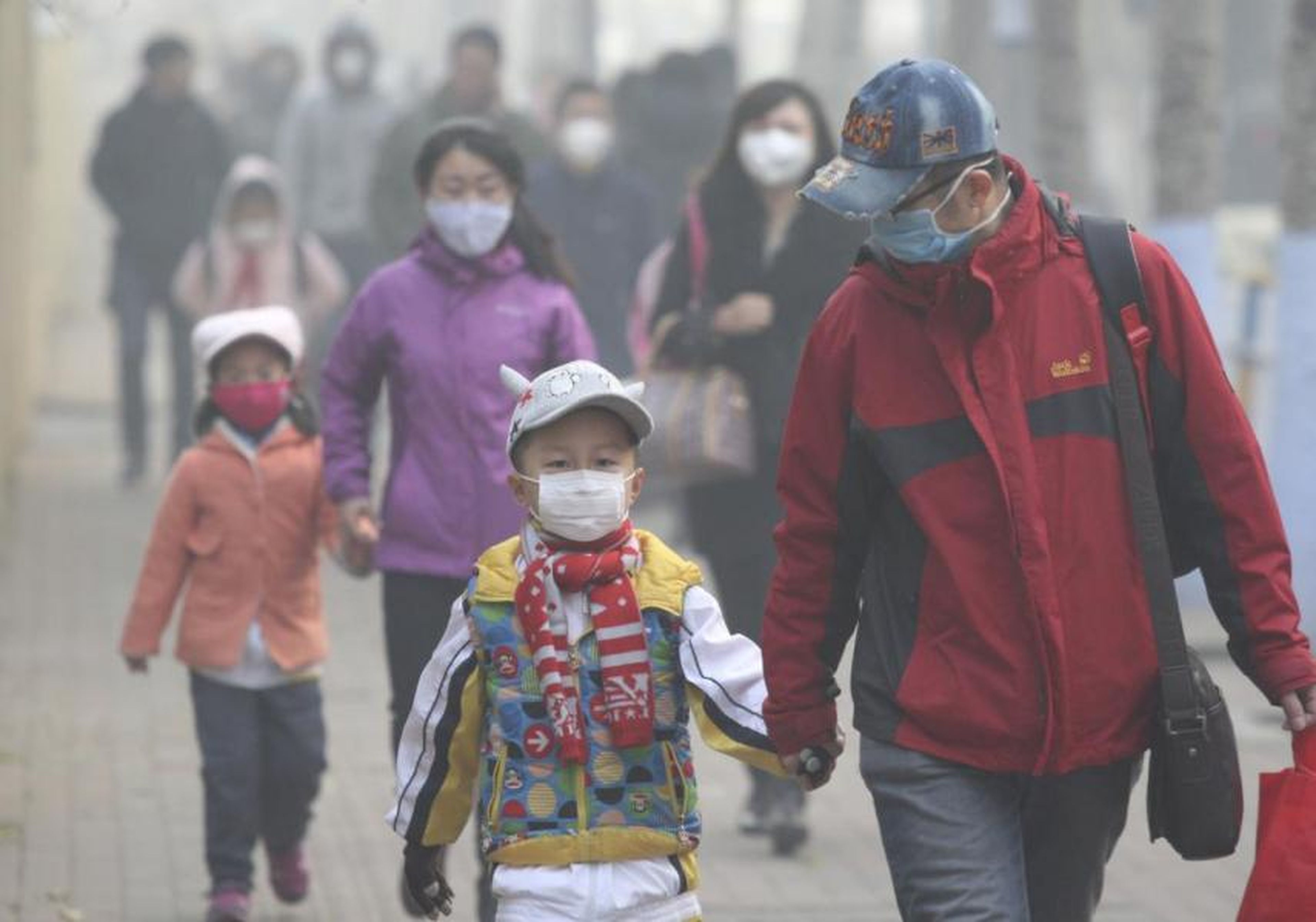 Jóvenes estudiantes y sus padres con máscaras caminan por una calle en un día nebuloso en Harbin, China, el 3 de noviembre de 2015.