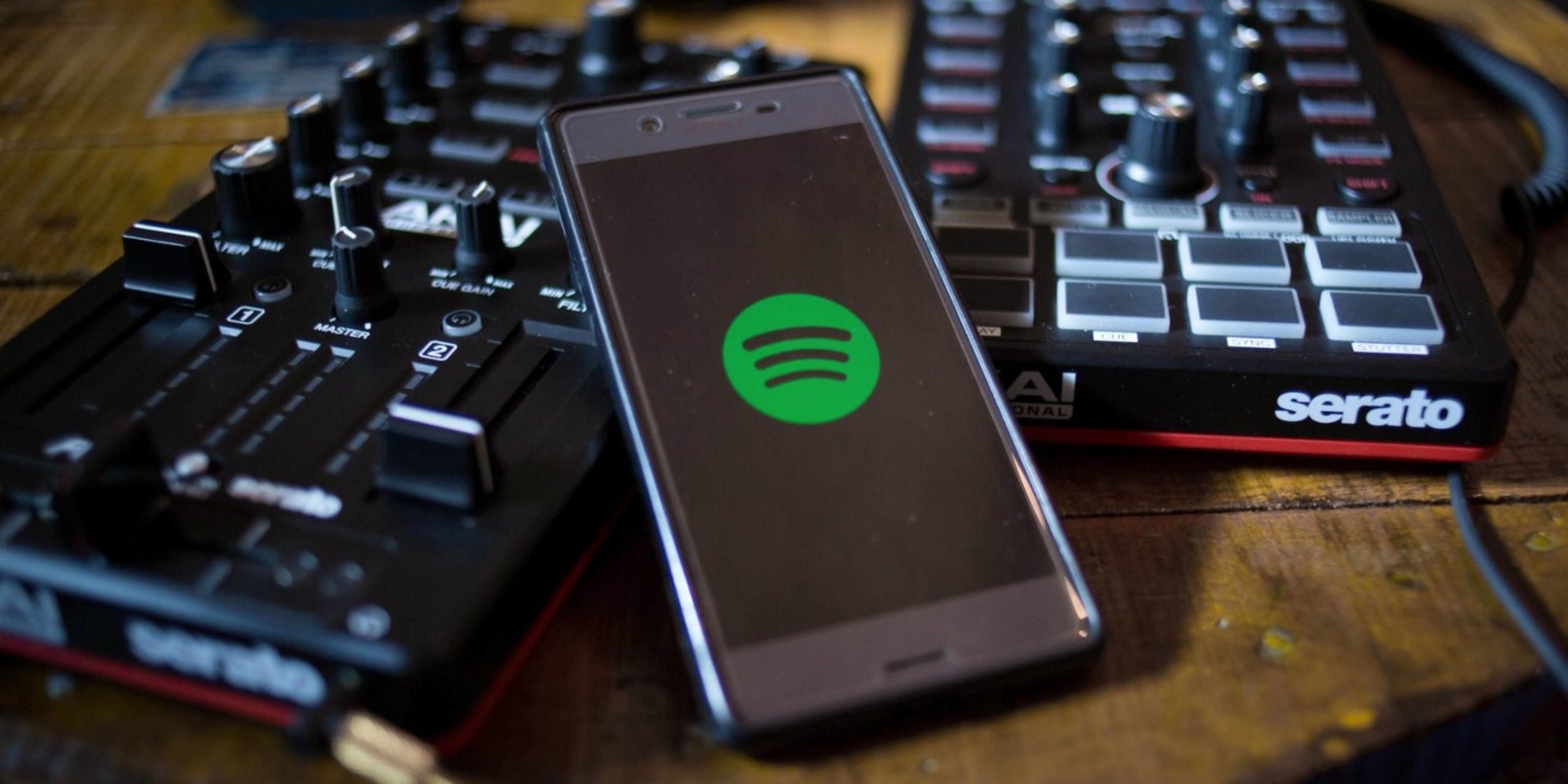 Un móvil con Spotify junto a dos mesas de mezcla de sonido
