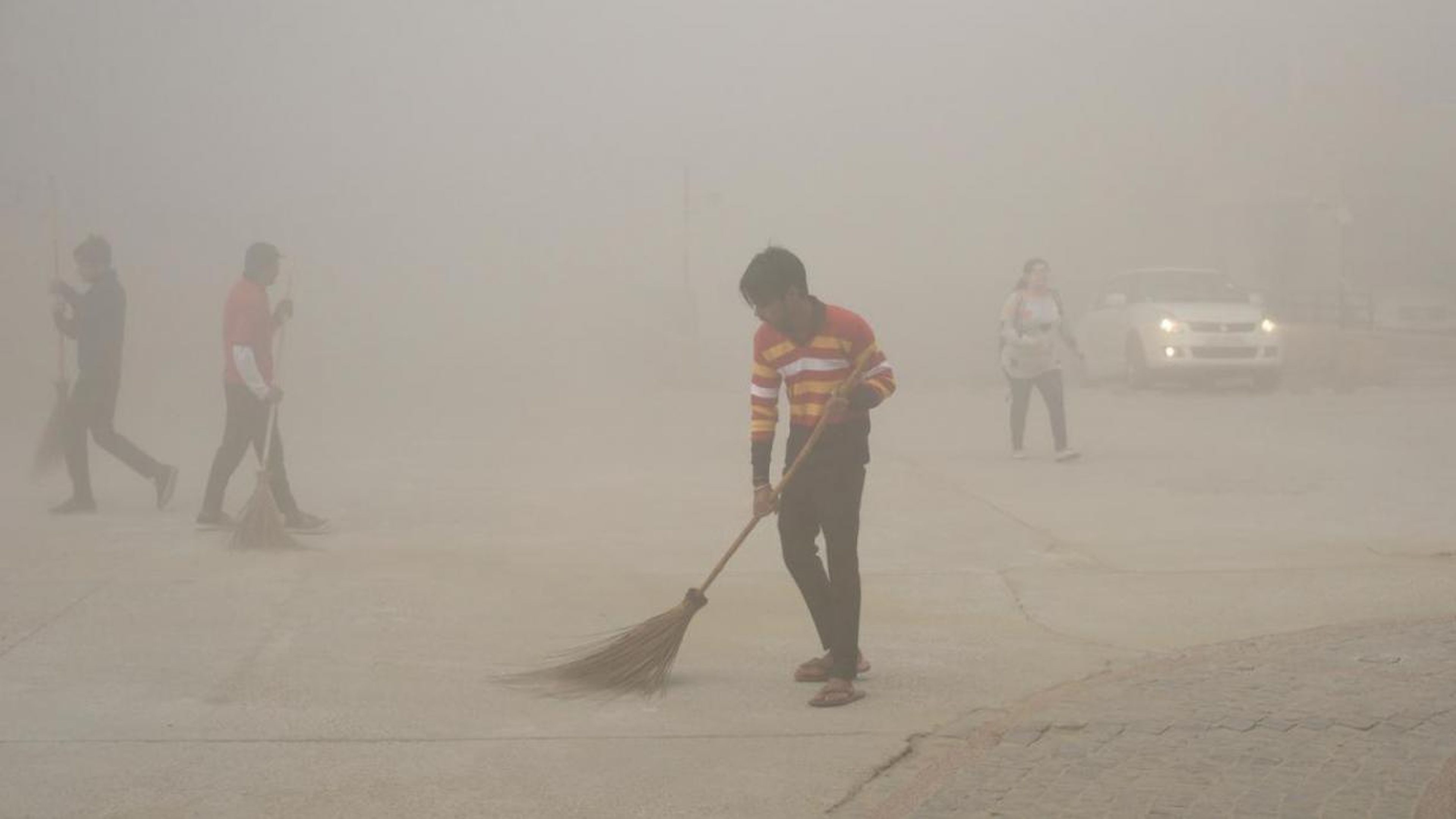 Trabajadores indios usan escobas para barrer el polvo en la niebla matutina en el Gran Noida, cerca de Nueva Delhi, India, el 10 de noviembre de 2017.
