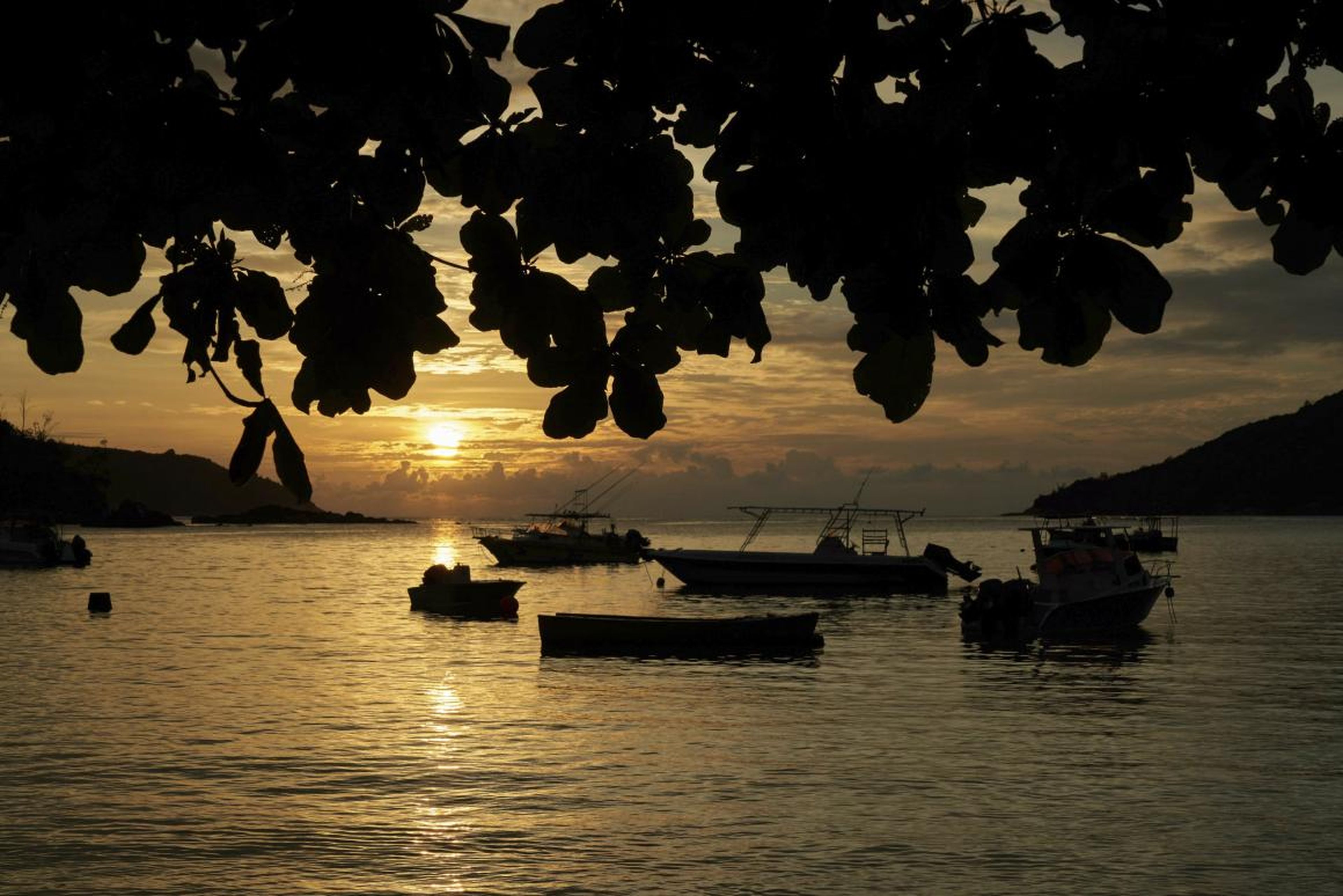 El sol se pone sobre una pequeña bahía pesquera con embarcaciones de recreo cerca de la isla de Mahe, Seychelles.