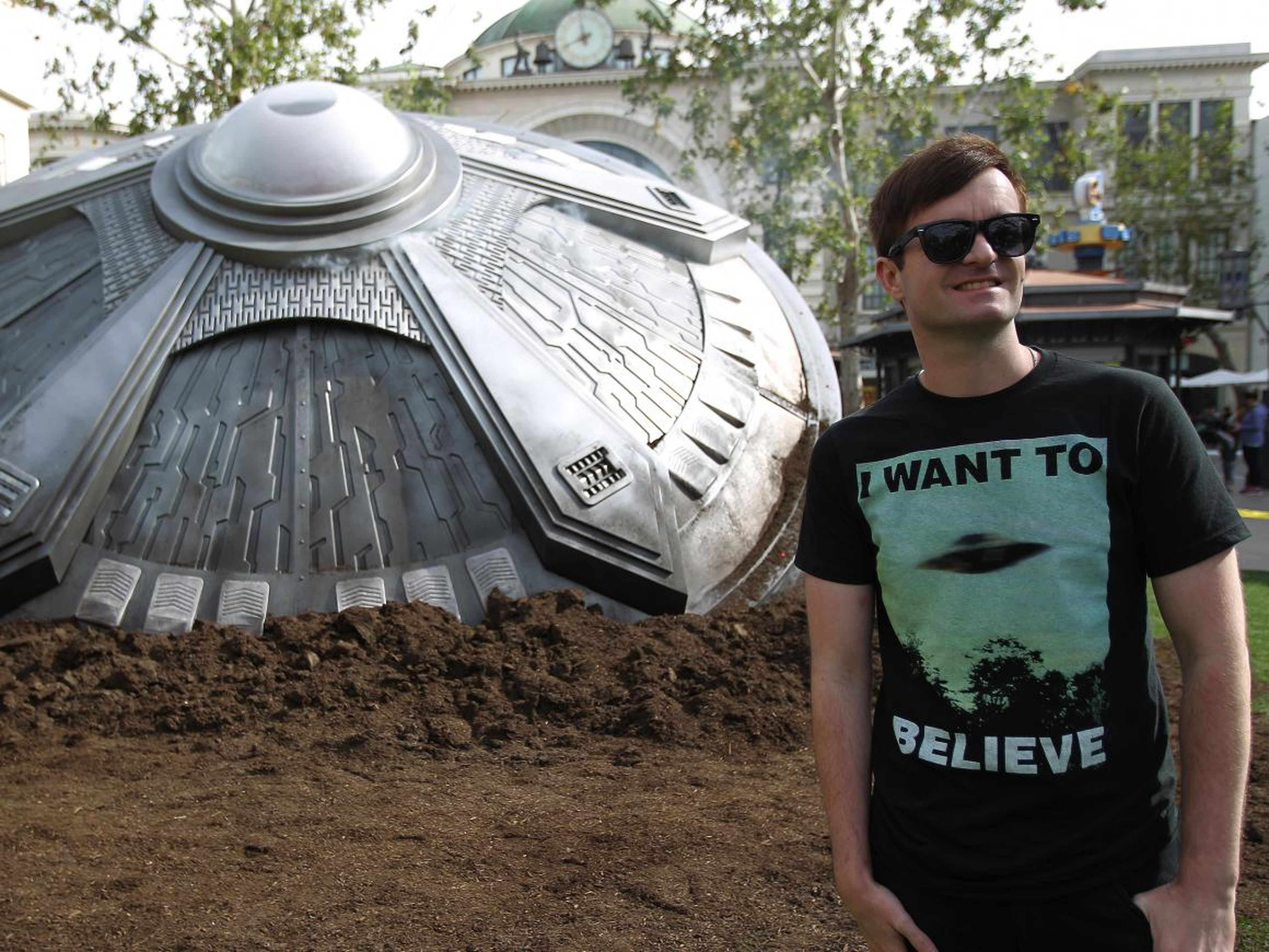 Fan wears "I want to believe" t-shirt in front of UFO model for Fox's "The X-Files" UFO episode.
