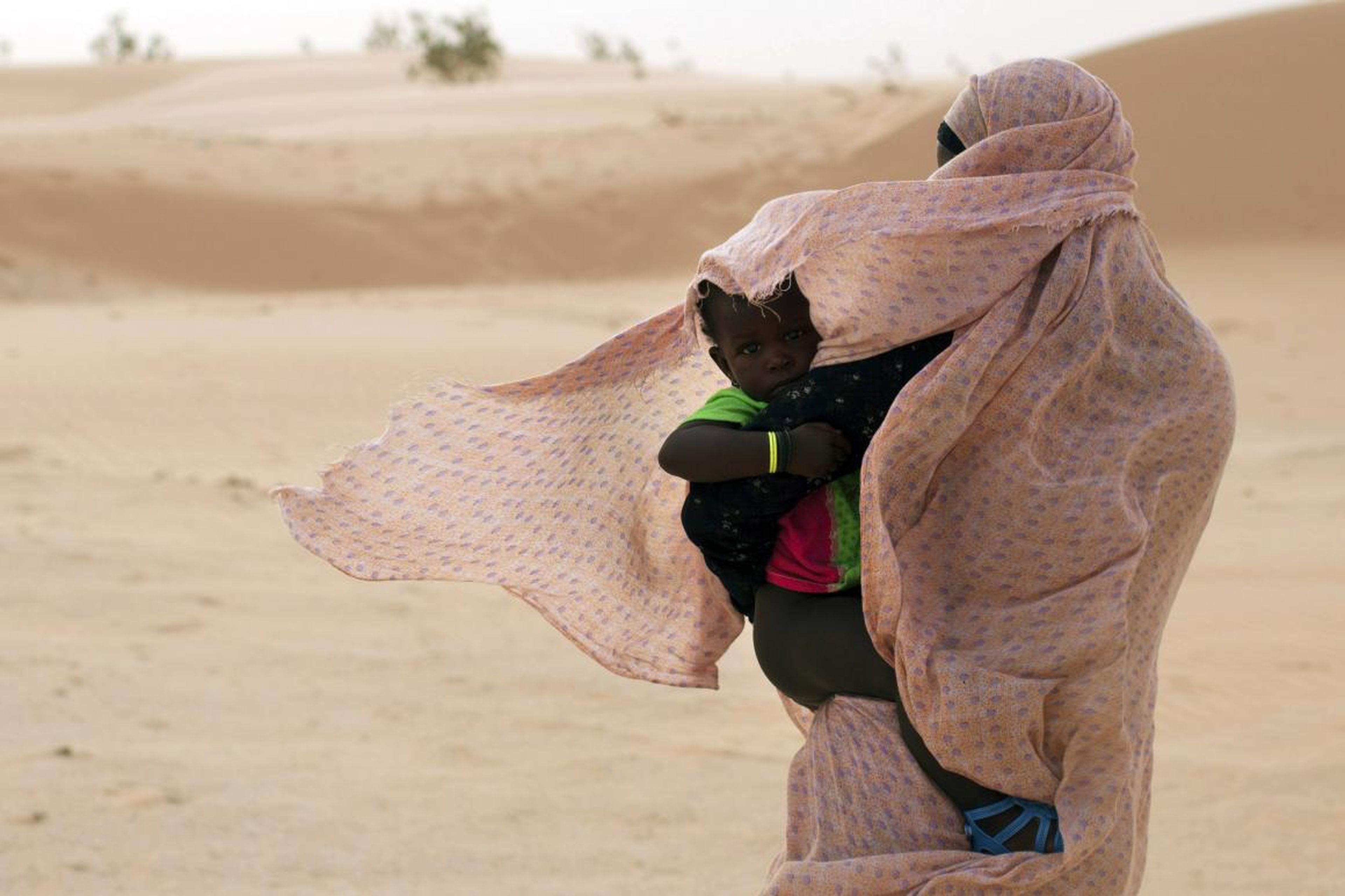 Una mujer protege a su hijo del viento mientras camina sobre las dunas de arena en Nouakchott, Mauritania.