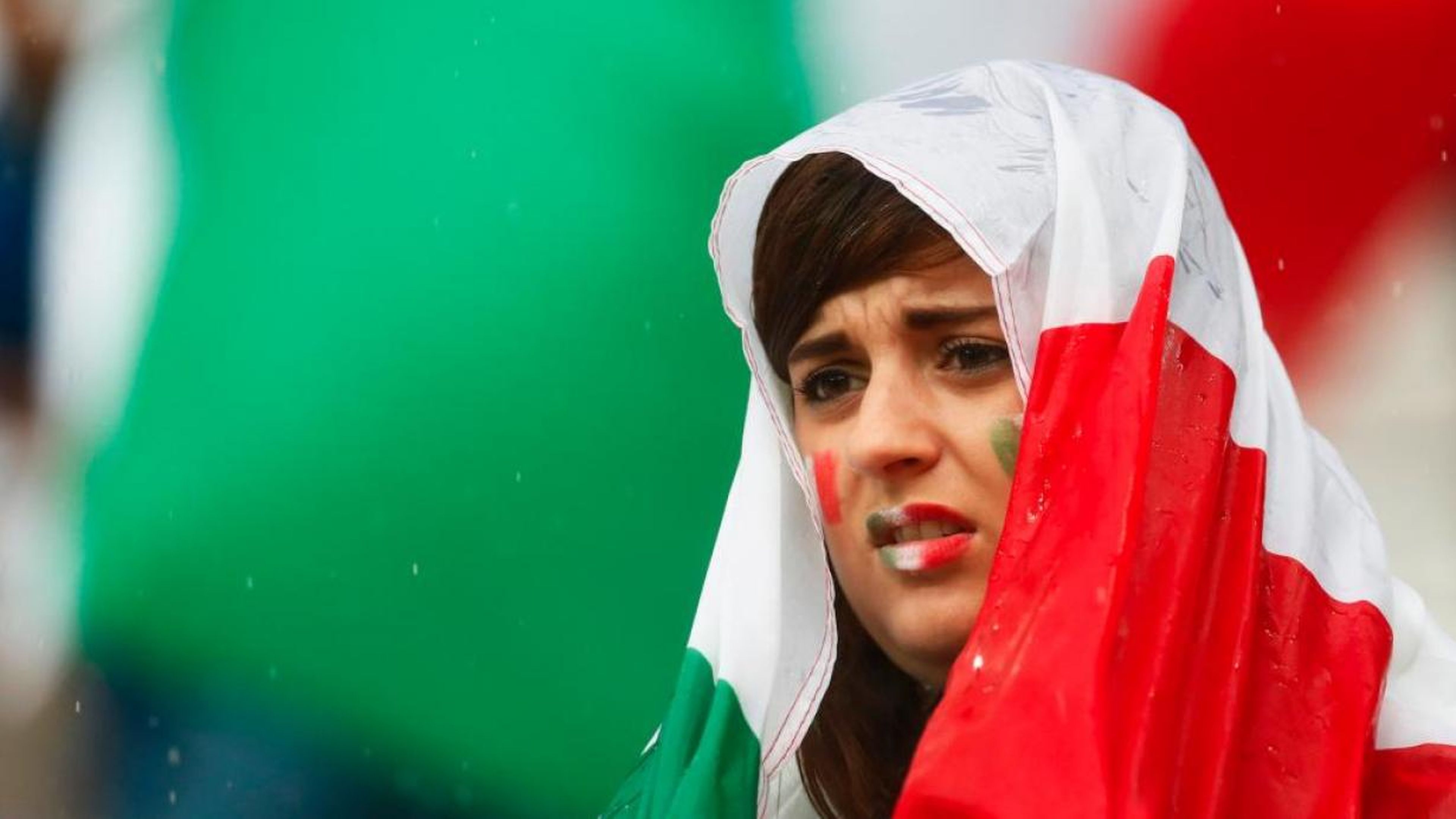 Una mujer ataviada con la bandera italiana mira con preocupación un partido de su selección de fútbol