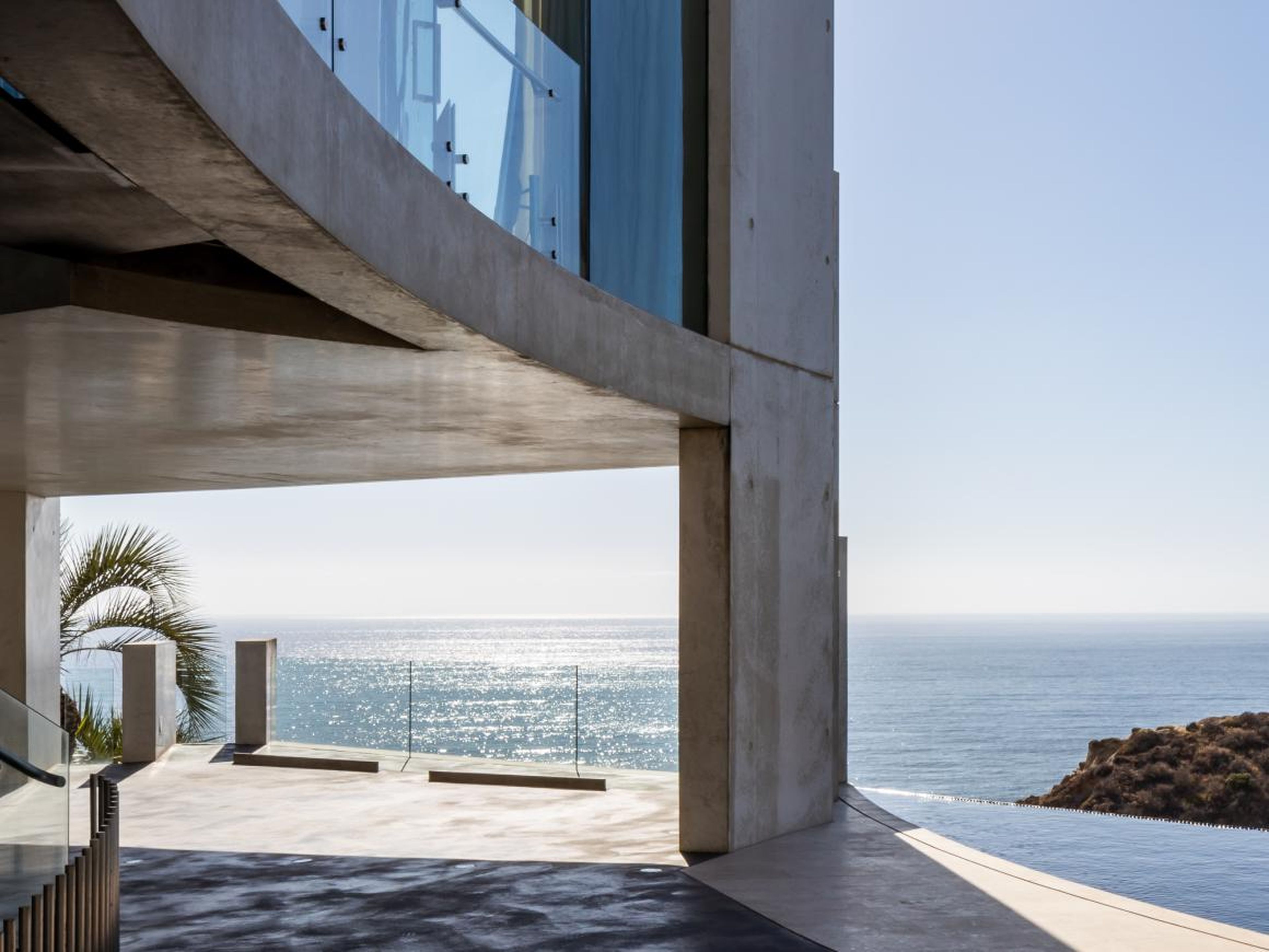 Perched on a cliff overlooking the Pacific Ocean, the home is made of white concrete, stainless steel supports, and floor-to-ceiling glass walls.