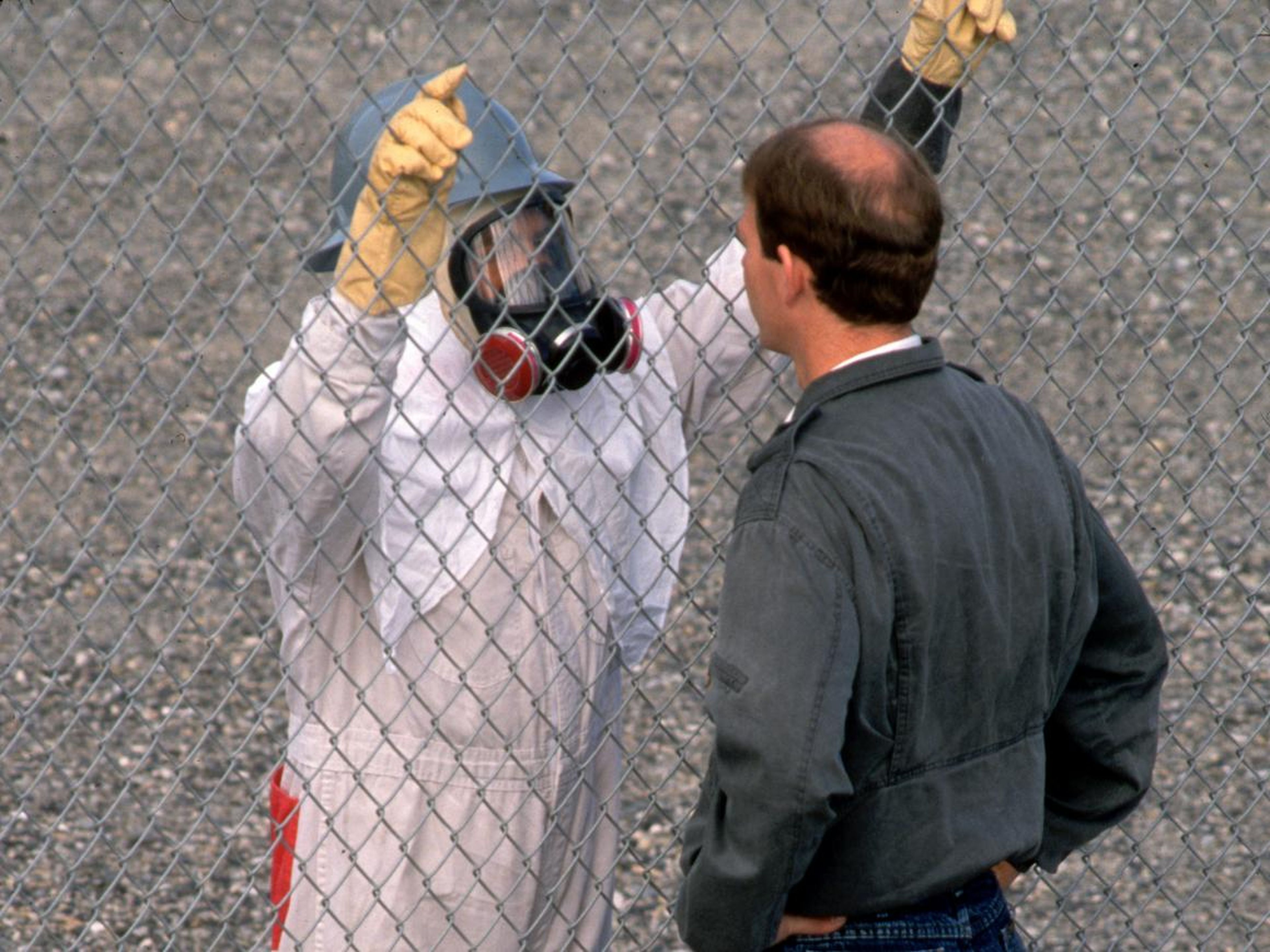 Un trabajador con un traje de radiación habla con un hombre a través de una valla de alambre.