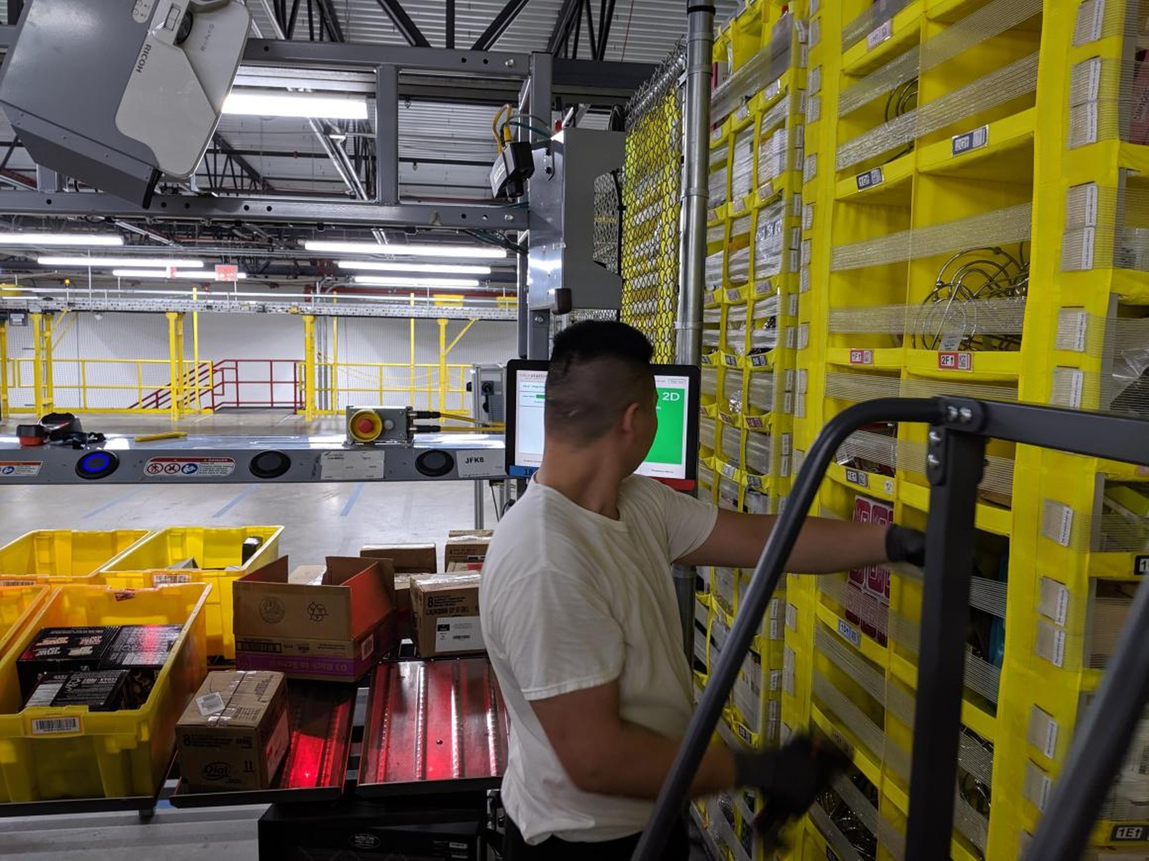 To this employee's left, totes come in full of products. Each item is scanned, which sets off a series of automated actions that guide the employee to where to place the item on the storage compartment.