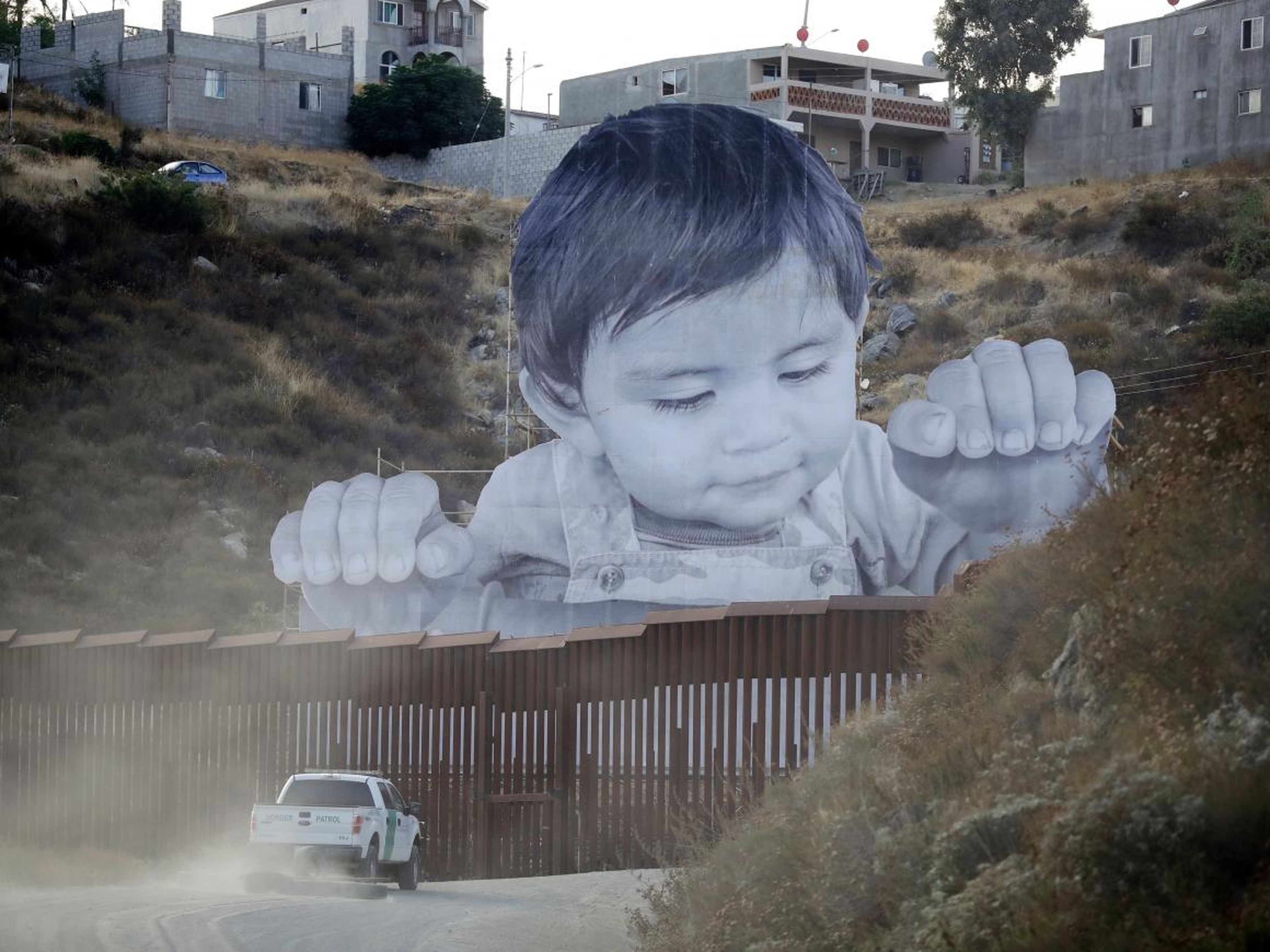 Un vehículo de la Patrulla Fronteriza conduce frente al mural de JR en Tecate, México, cerca de Tecate, California, en 2017.