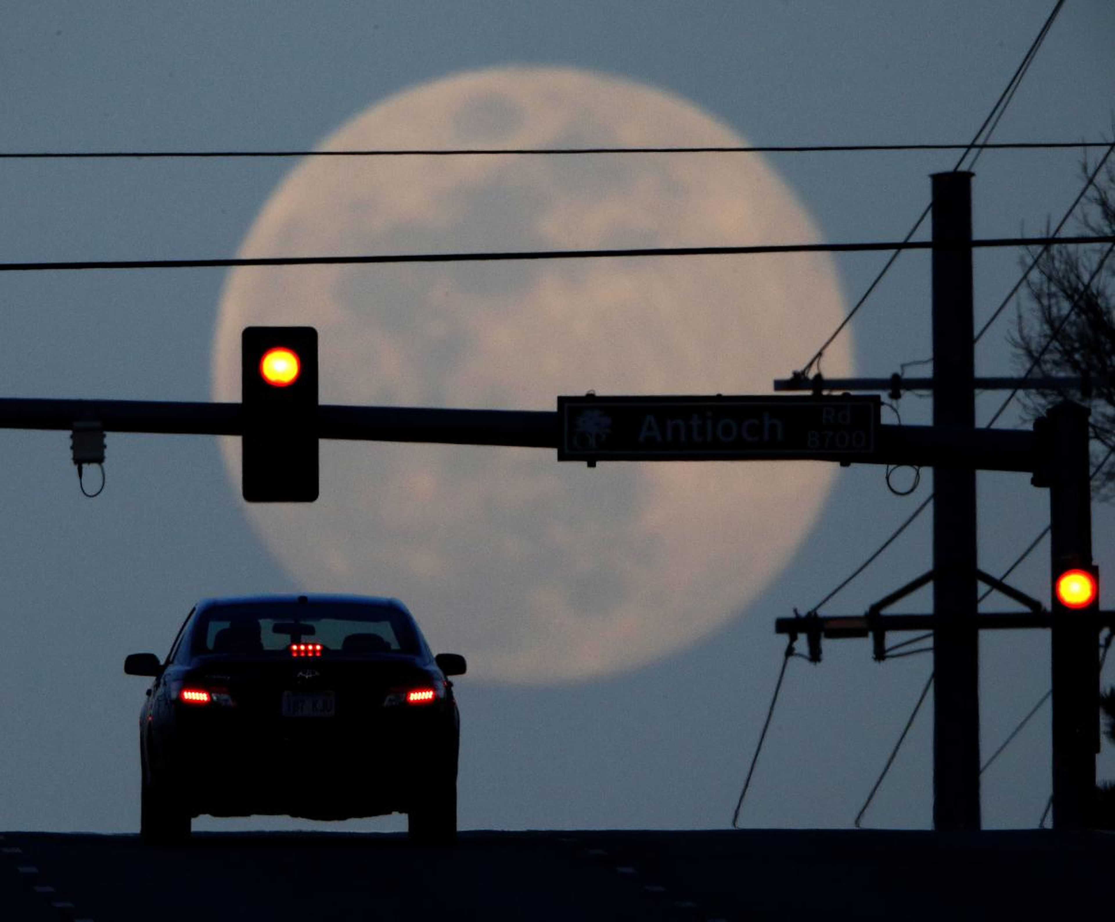En esta foto del 30 de marzo de 2018, un automovilista espera en un semáforo mientras la luna llena se eleva en Overland Park, Kansas.