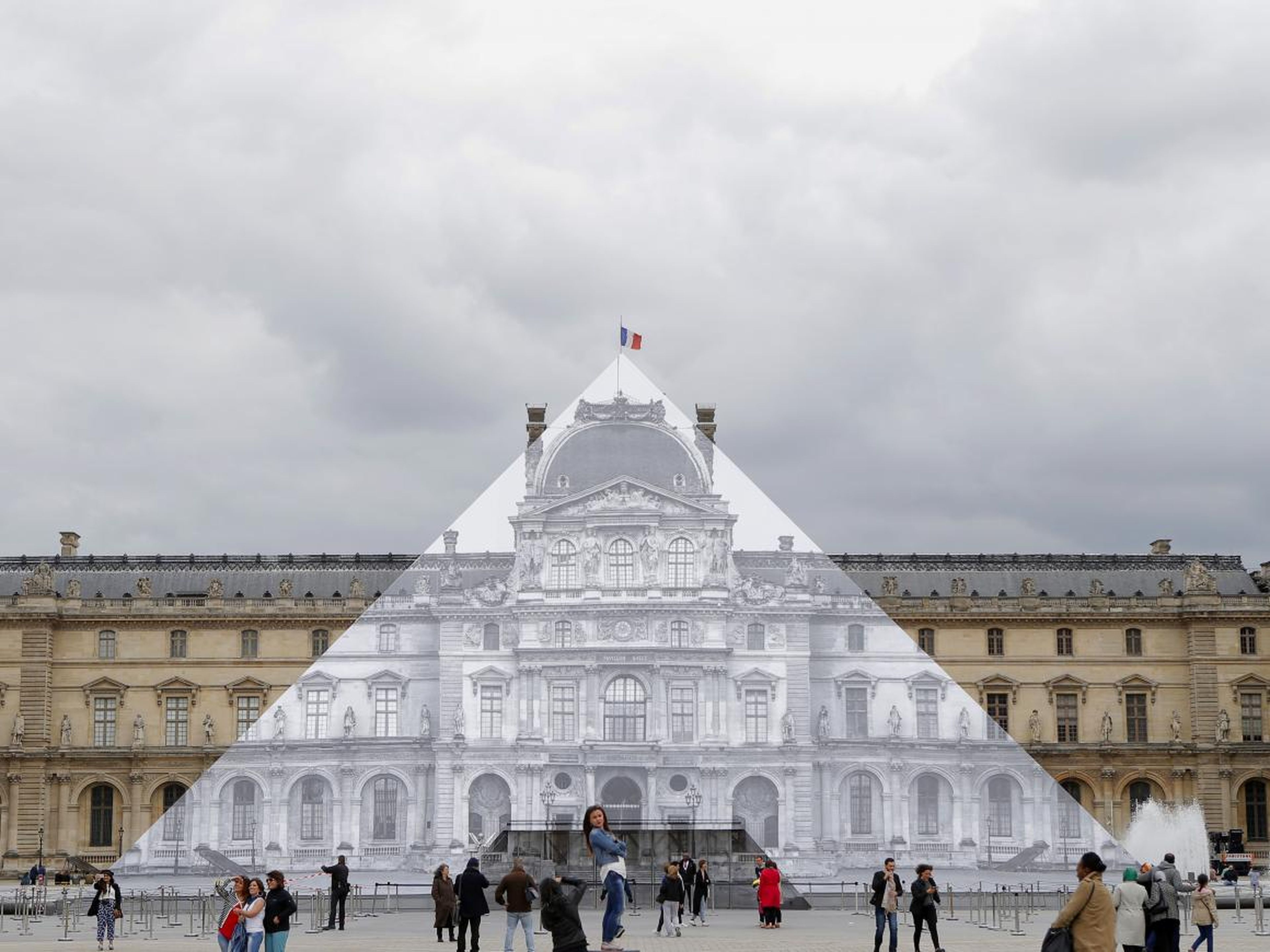 Los turistas caminan alrededor del proyecto JR en el Louvre en París, Francia, en 2016.
