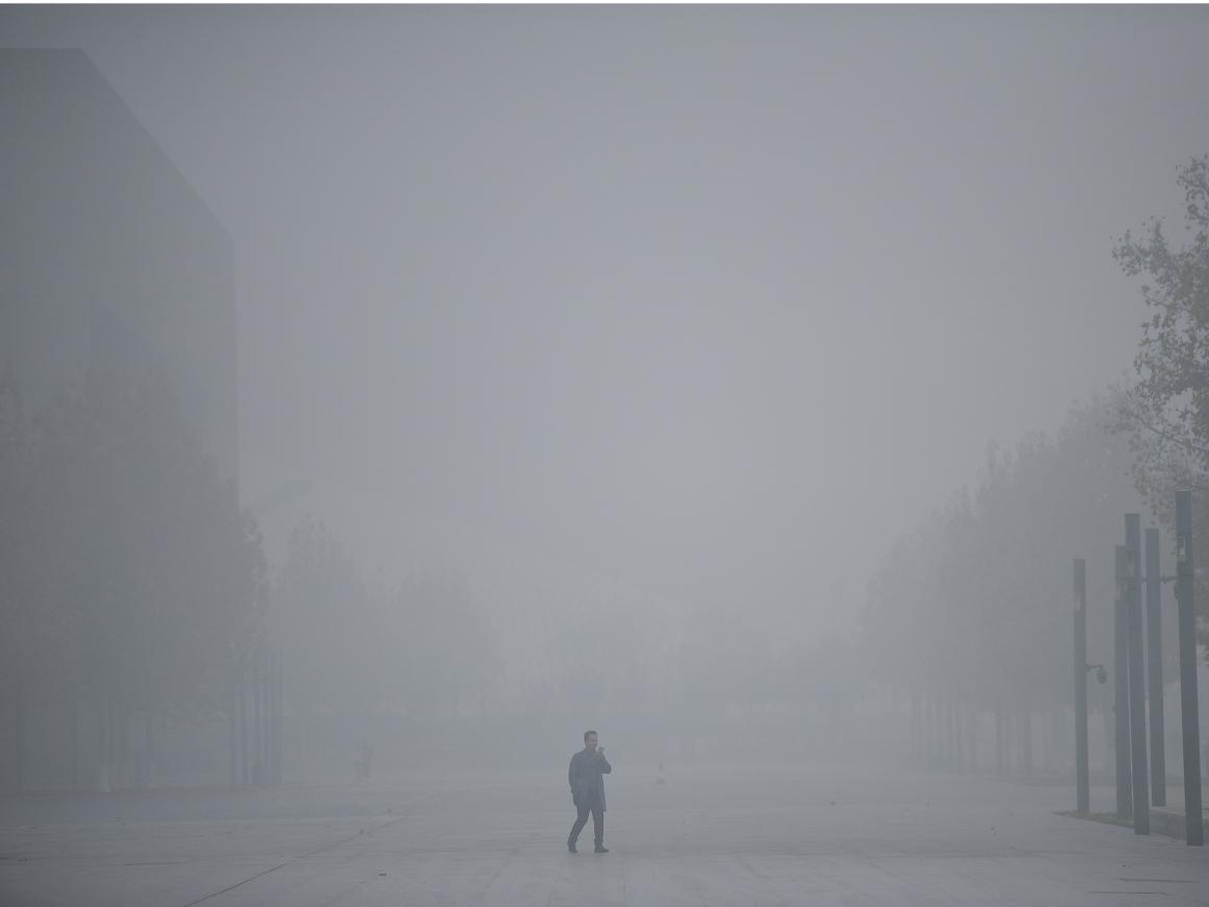 Un hombre utiliza su móvil mientras camina entre el 'smog' en Tianjin, China.