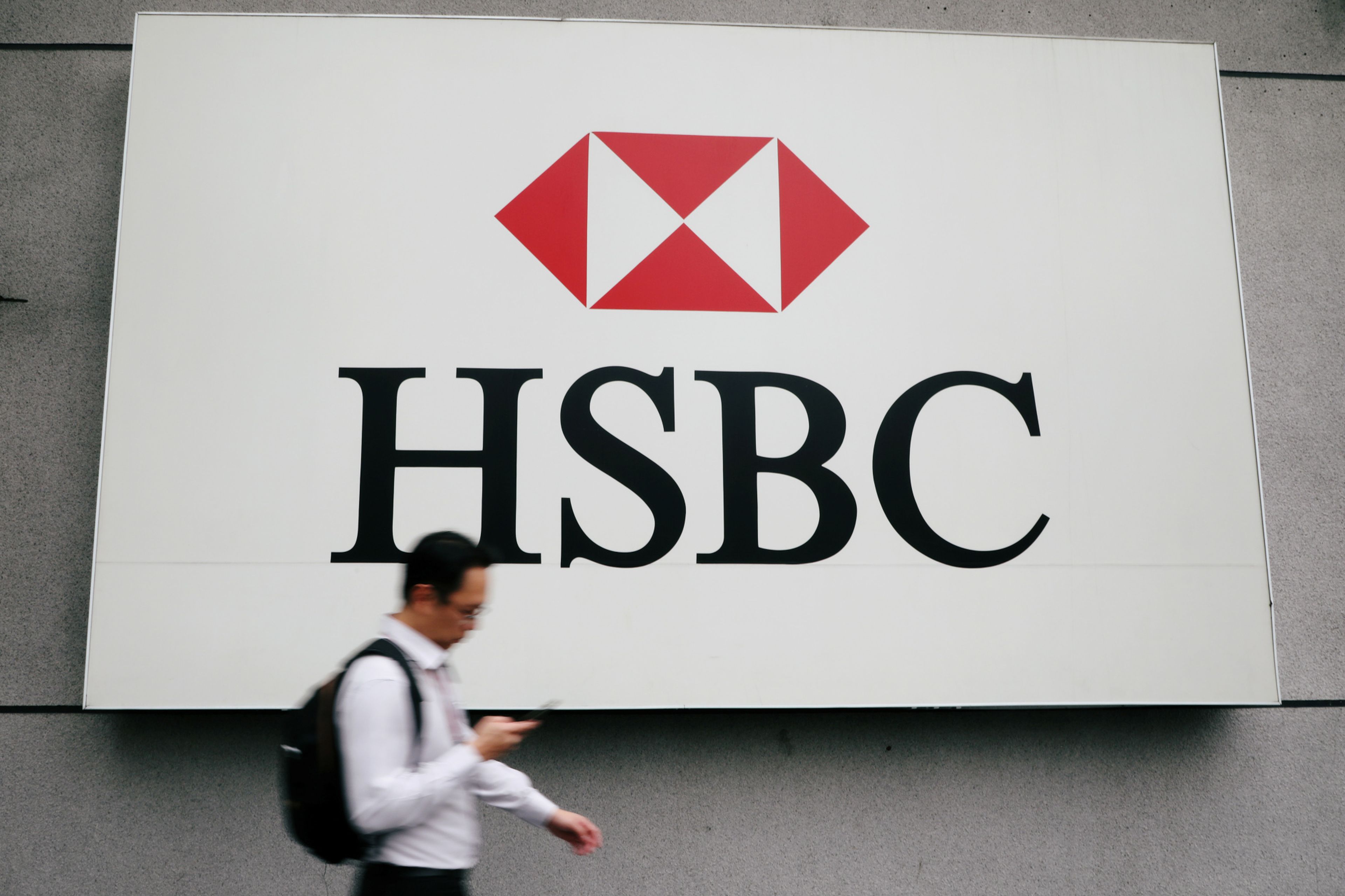 Un hombre camina delante de un cartel de HSBC.