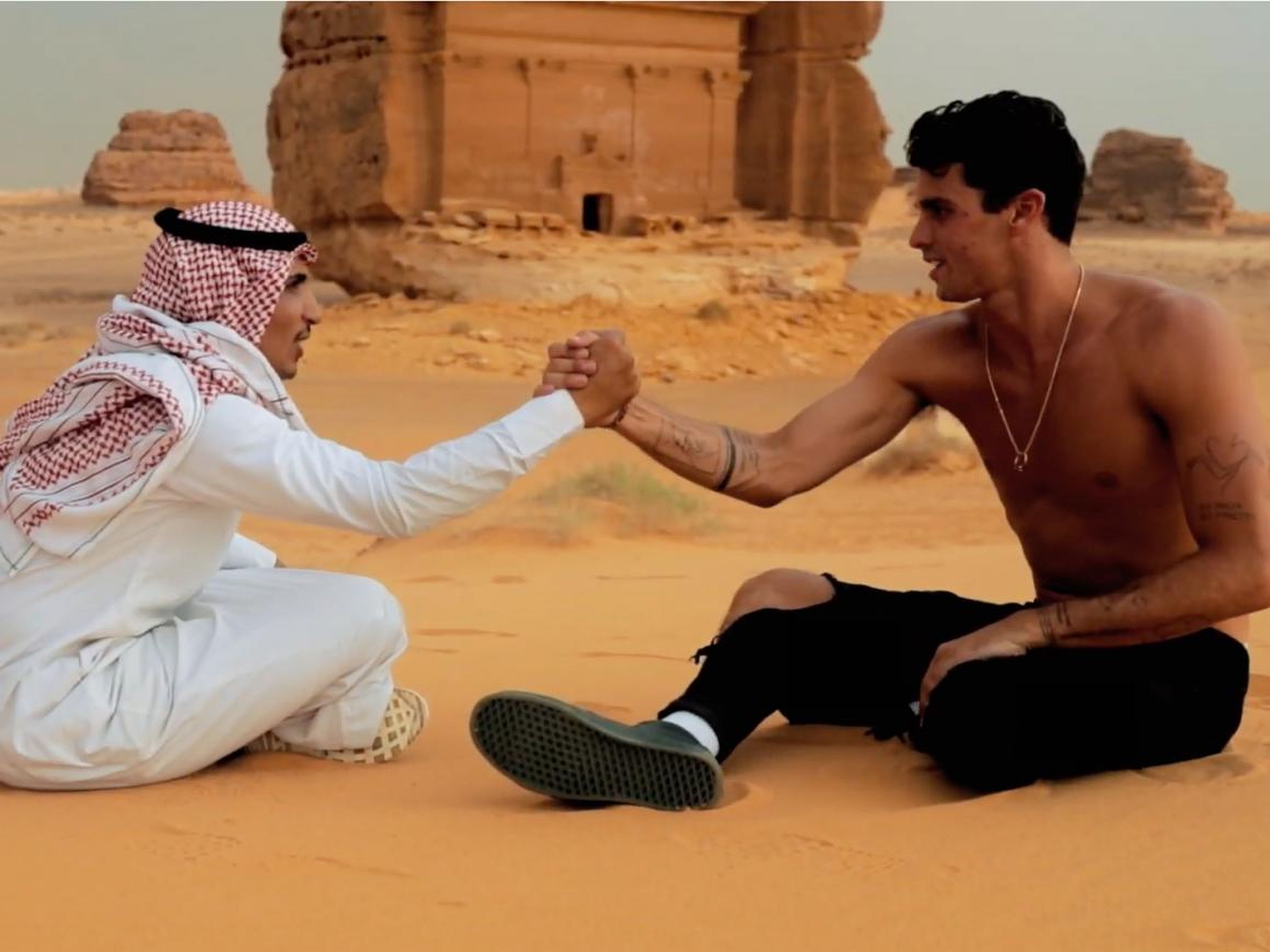 La megaestrella de Instagram Jay Alvarez le da la mano a un hombre saudí que lleva un keffiyeh y thawb en el centro de patrimonio de Arabia Saudí Mada'in Saleh.
