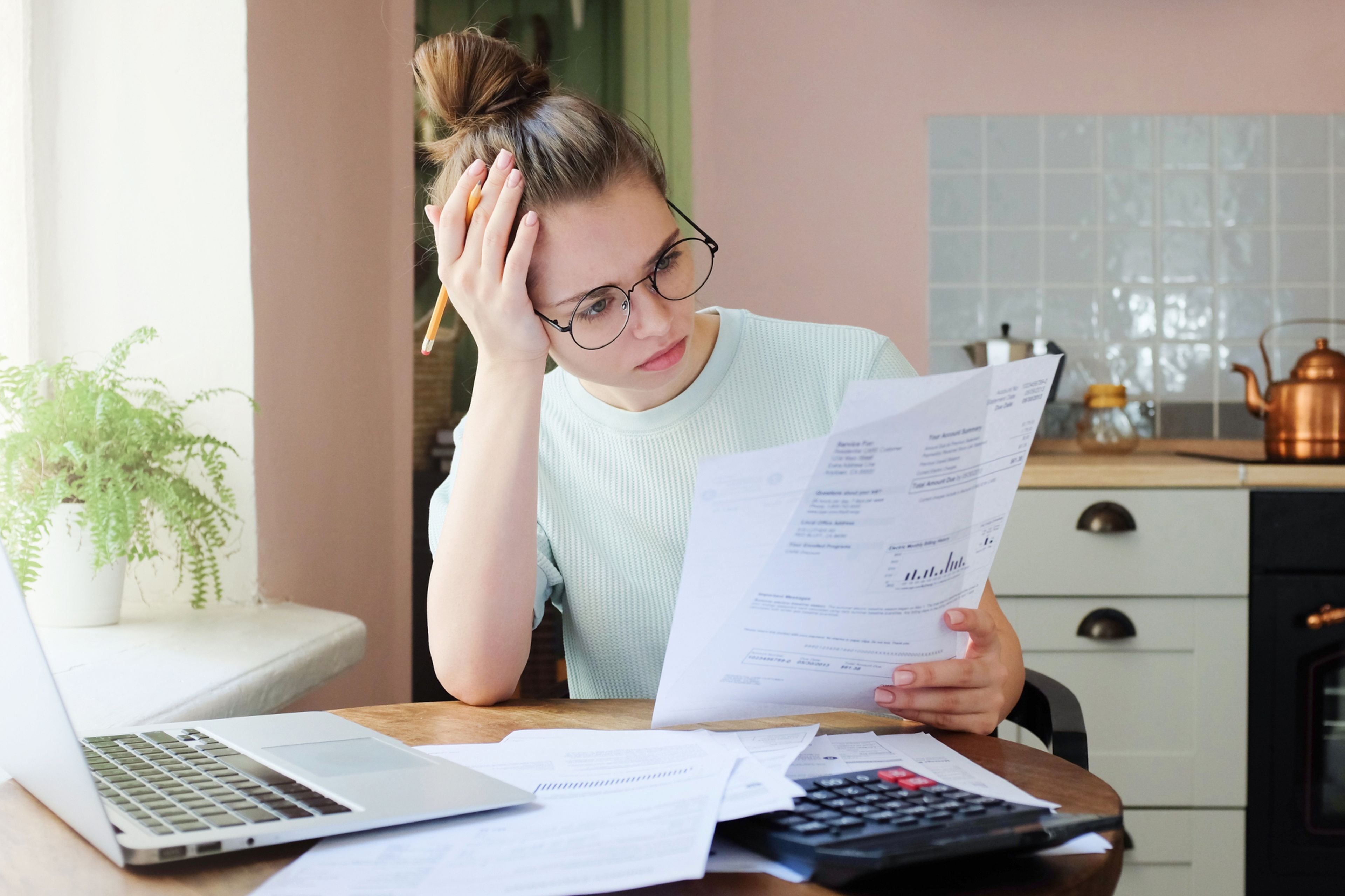 Una joven revisa facturas con un ordenador y una calculadora