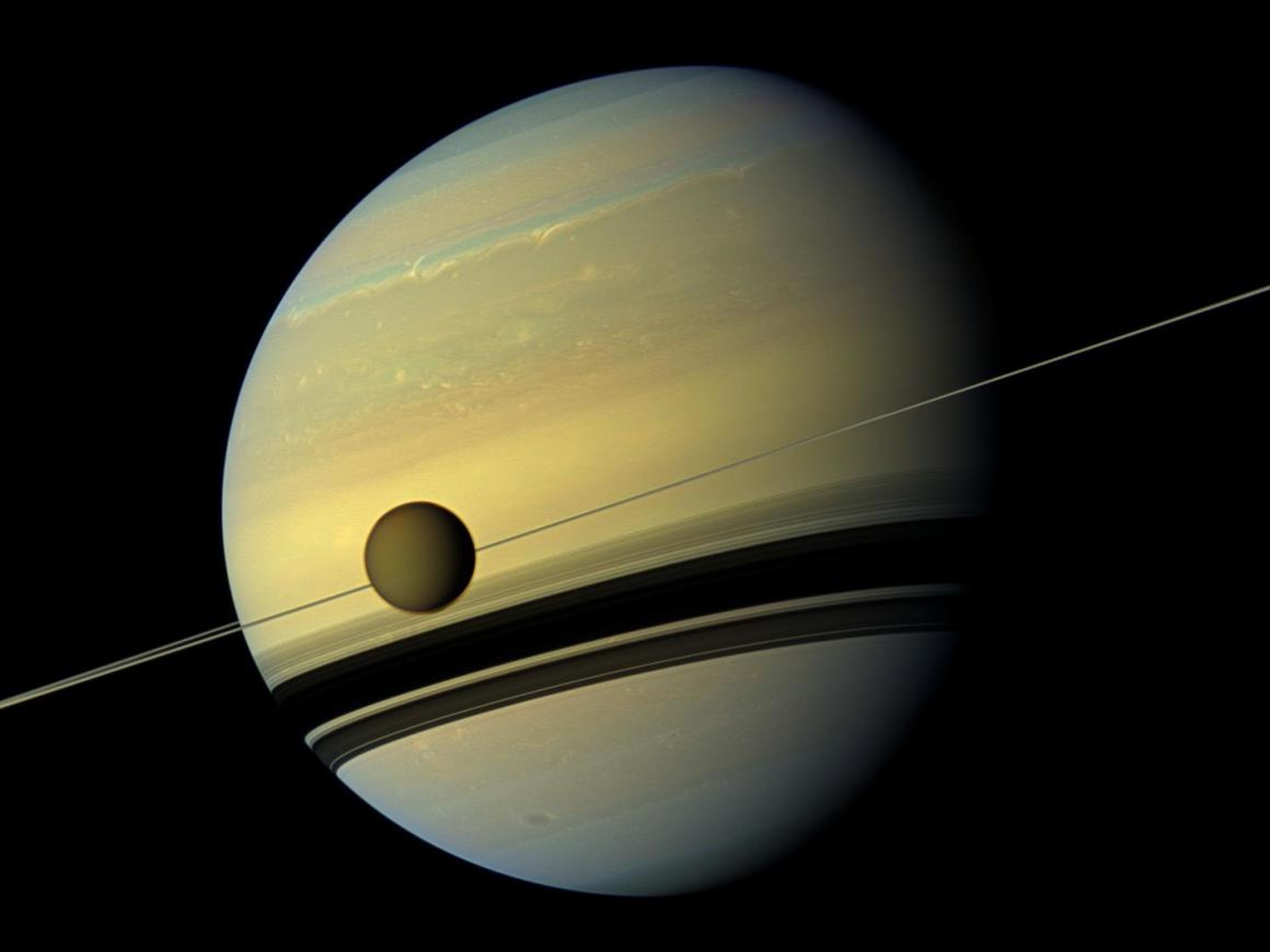 Saturn's largest moon, Titan, passes the planet undergoing seasonal changes in this natural color view from NASA's Cassini spacecraft.