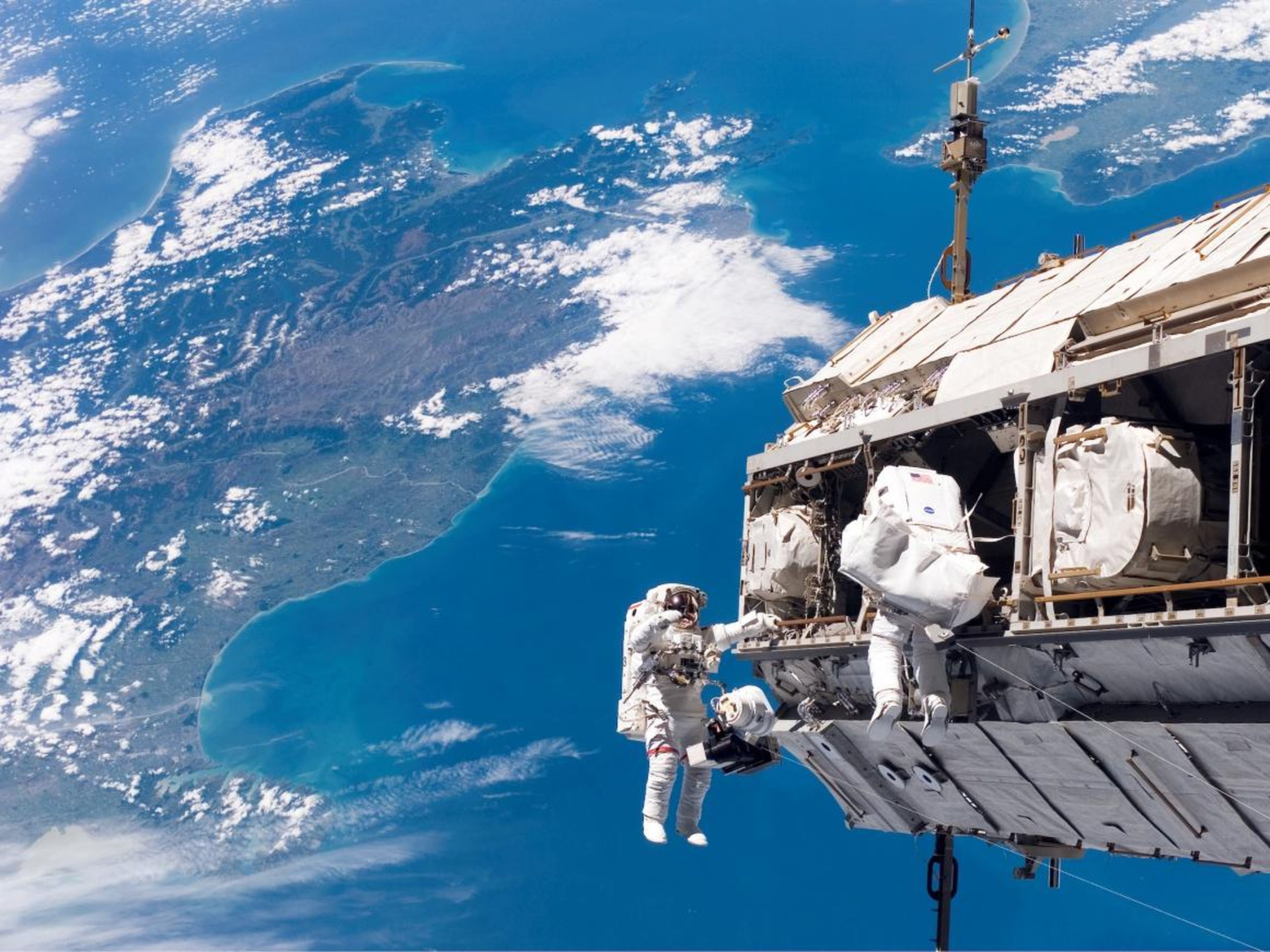 Backdropped by New Zealand and the Cook Strait in the Pacific Ocean, astronauts Robert L. Curbeam Jr. (left) and Christer Fuglesang (right) participate in an extravehicular activity (EVA).