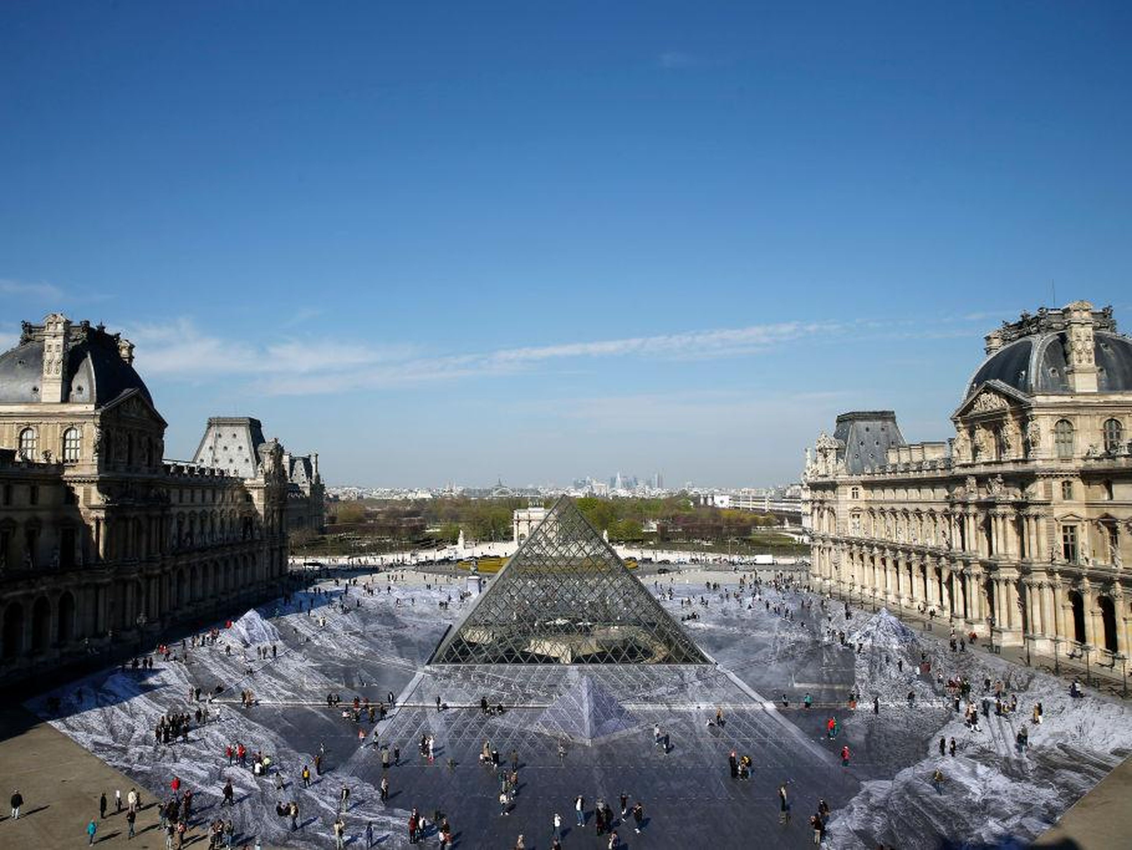 Los turistas caminan sobre una obra fotográfica gigante de JR en el patio principal del Museo del Louvre.