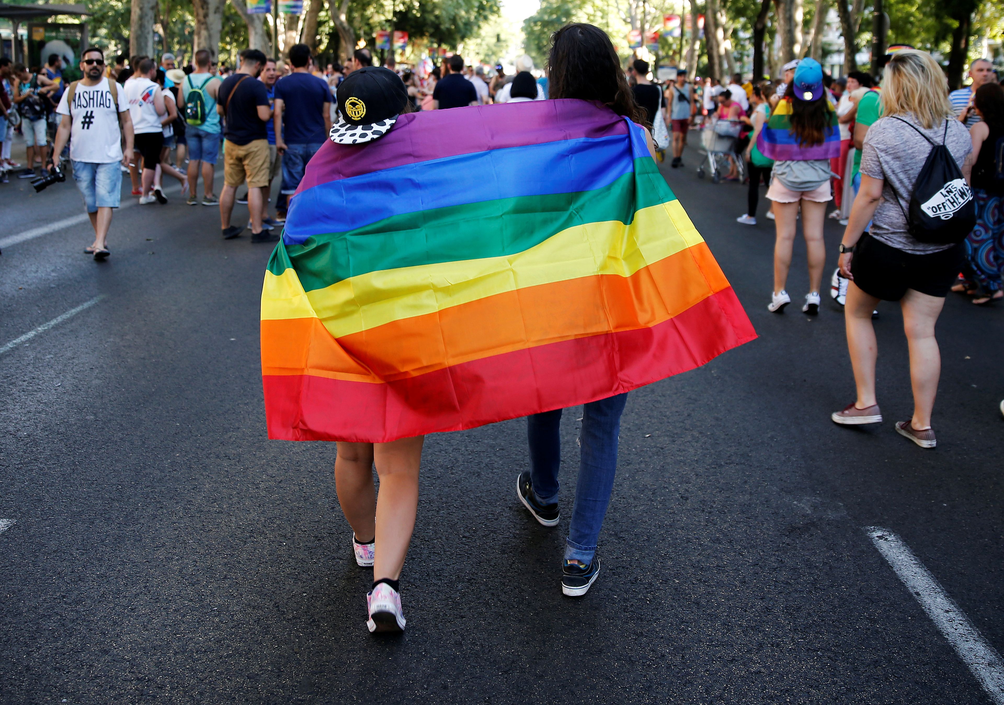 Una pareja pasea por el Paseo del Prado de Madrid con la bandera Gay.