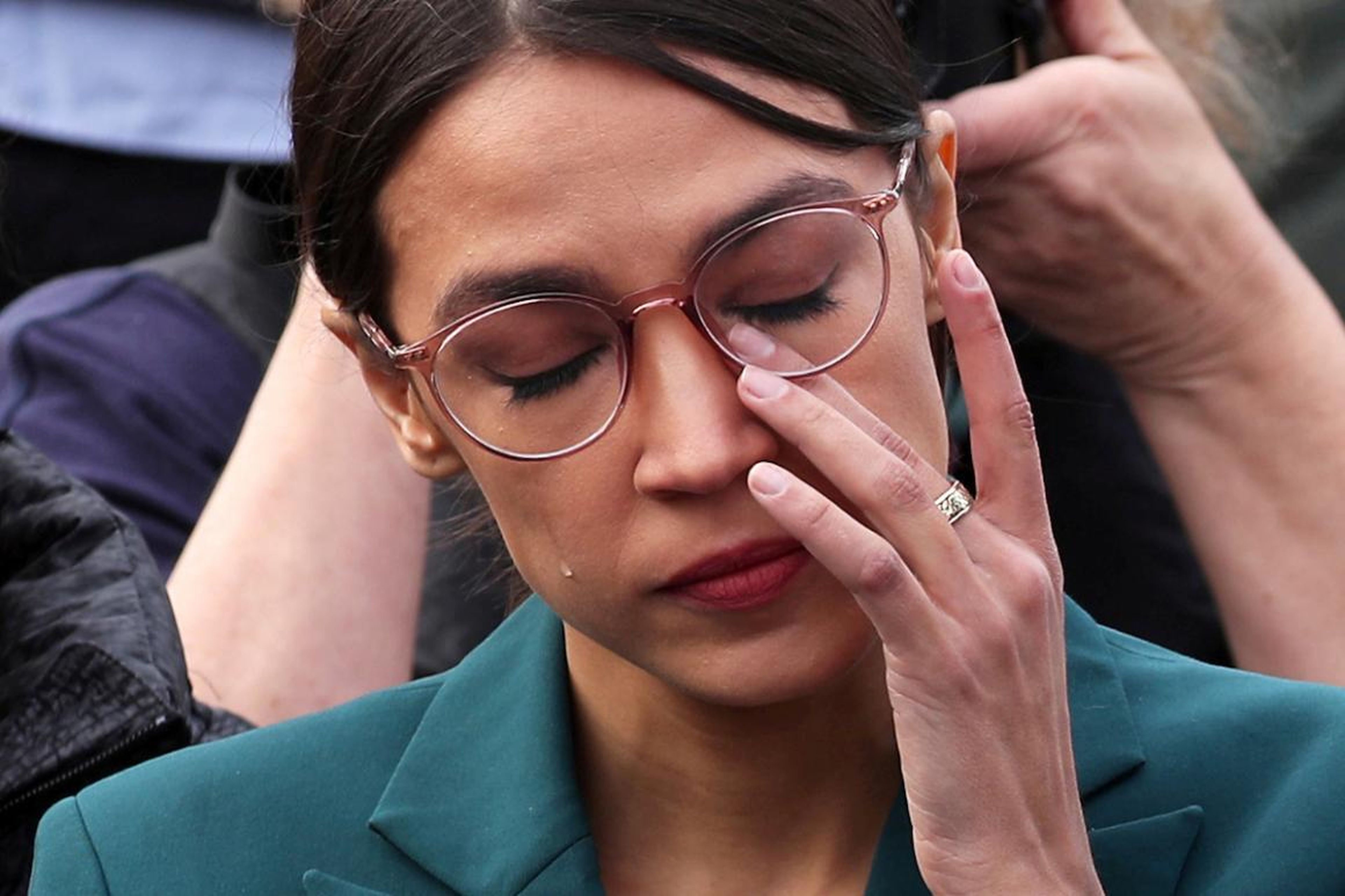 U.S. Representative Alexandria Ocasio-Cortez wipes away tears as Representative Ilhan Omar talks about her own experience as a refugee during a news conference calling on Congress to cut funding for ICE (Immigration and Customs