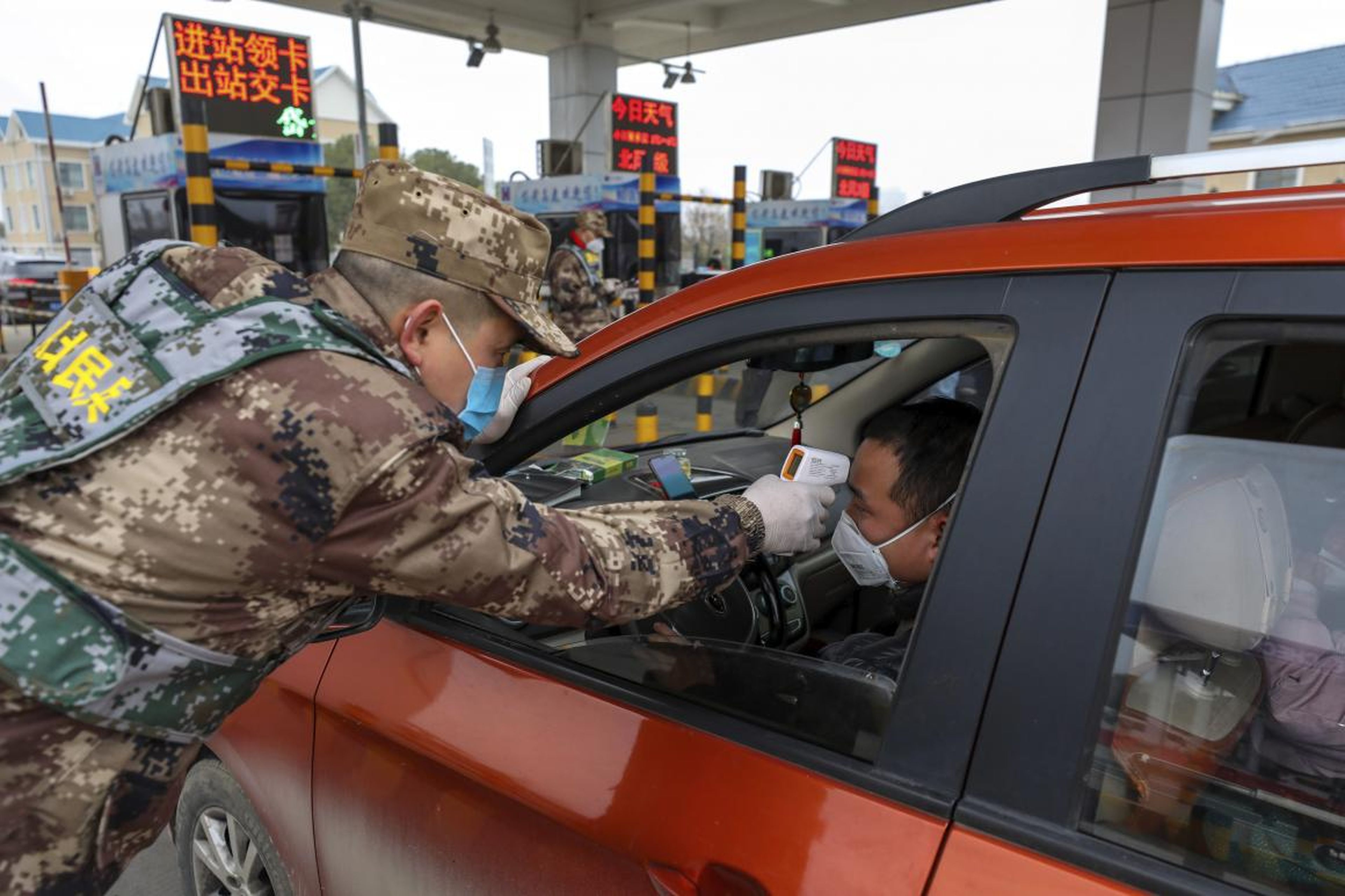 A militia member uses a digital thermometer to take a driver's temperature at a checkpoint at a highway toll gate in Wuhan, China, January 23, 2020.